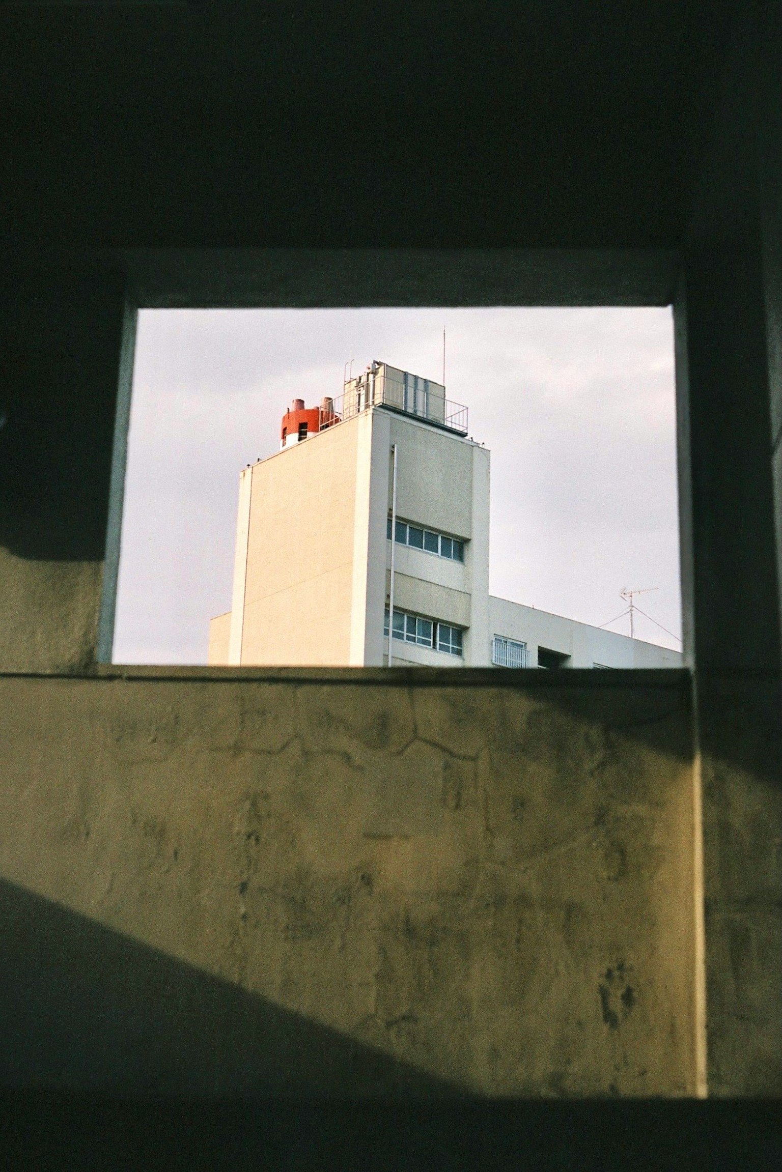 Blick auf ein Gebäude durch einen Fensterrahmen mit bewölktem Himmel