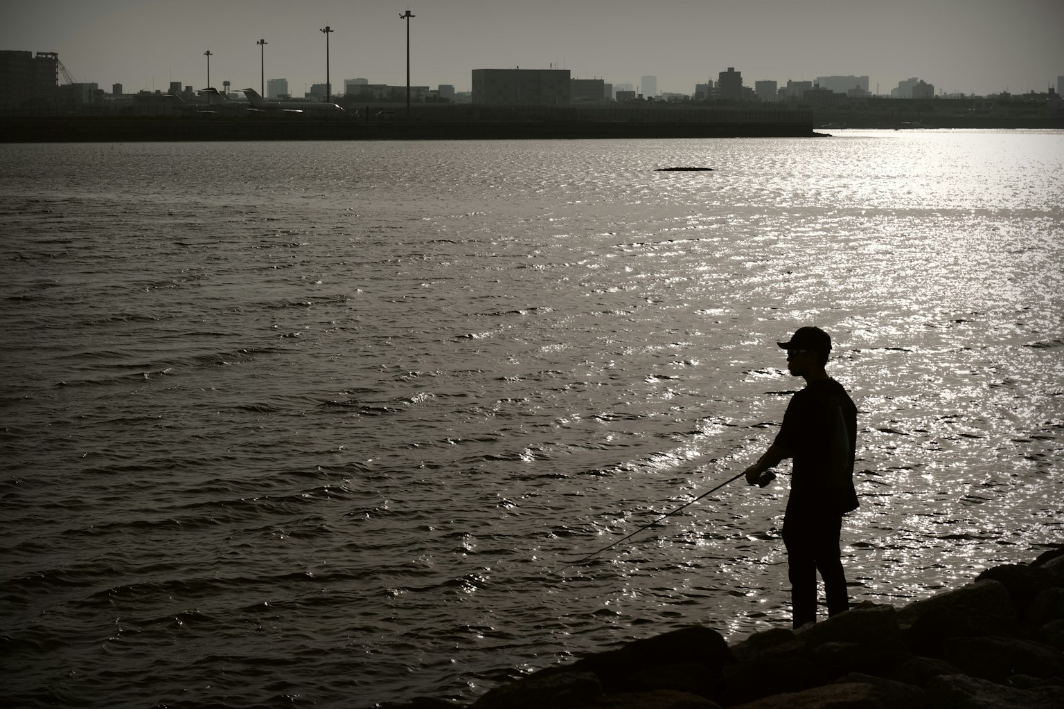 Silhouette eines Mannes, der die Wasseroberfläche mit einer städtischen Kulisse betrachtet