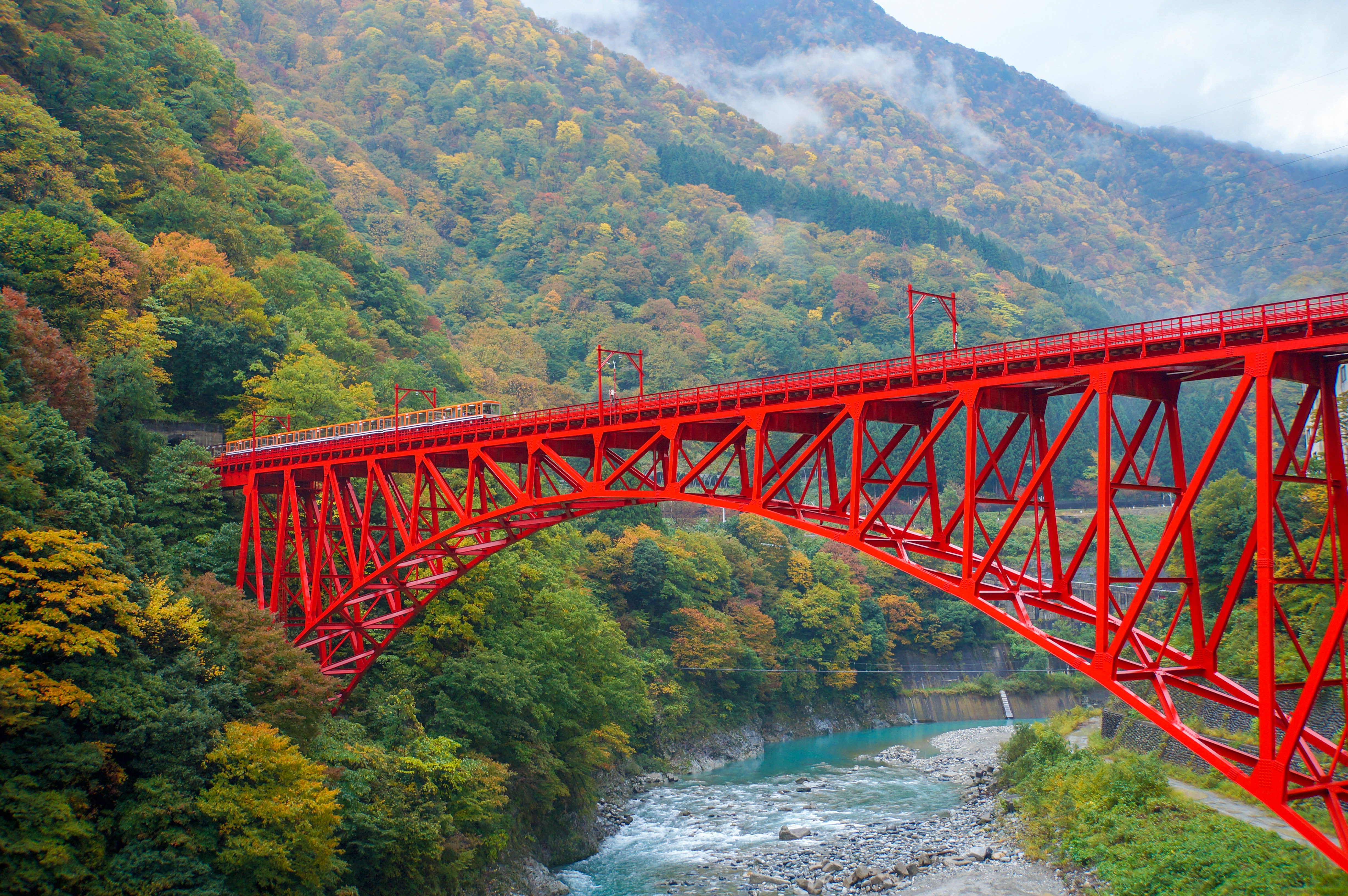 Red truss bridge over a river in a mountainous valley
