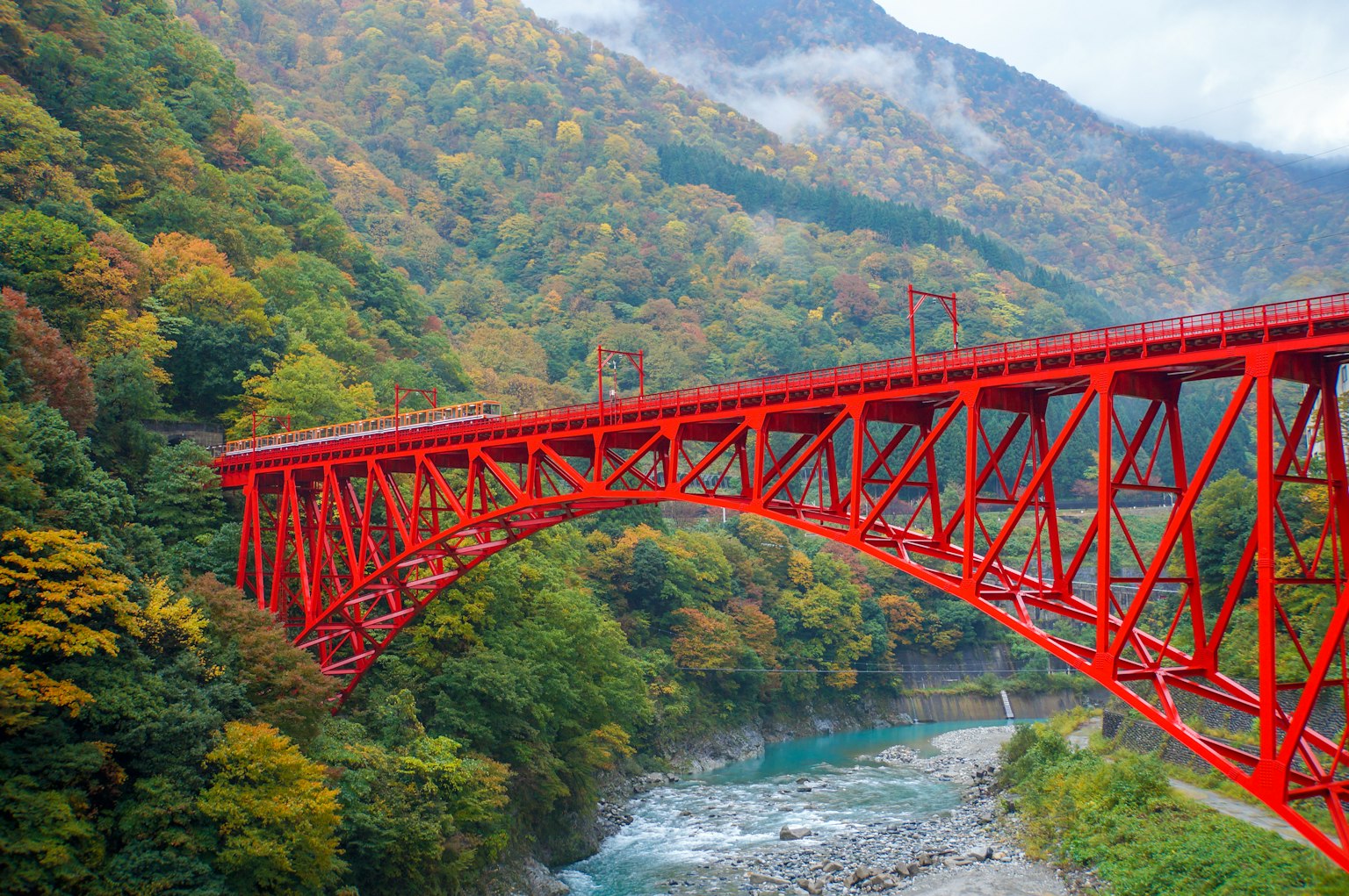 Red iron bridge in autumn landscape with green mountains
