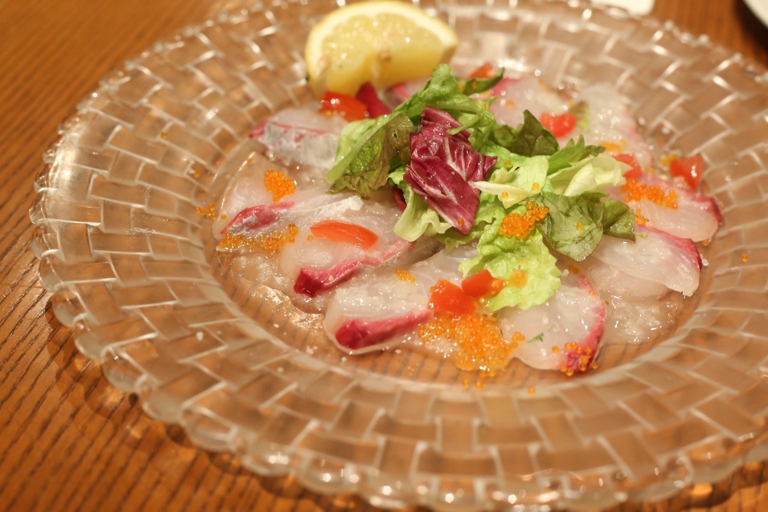 Sliced fish and vegetables arranged on a clear plate