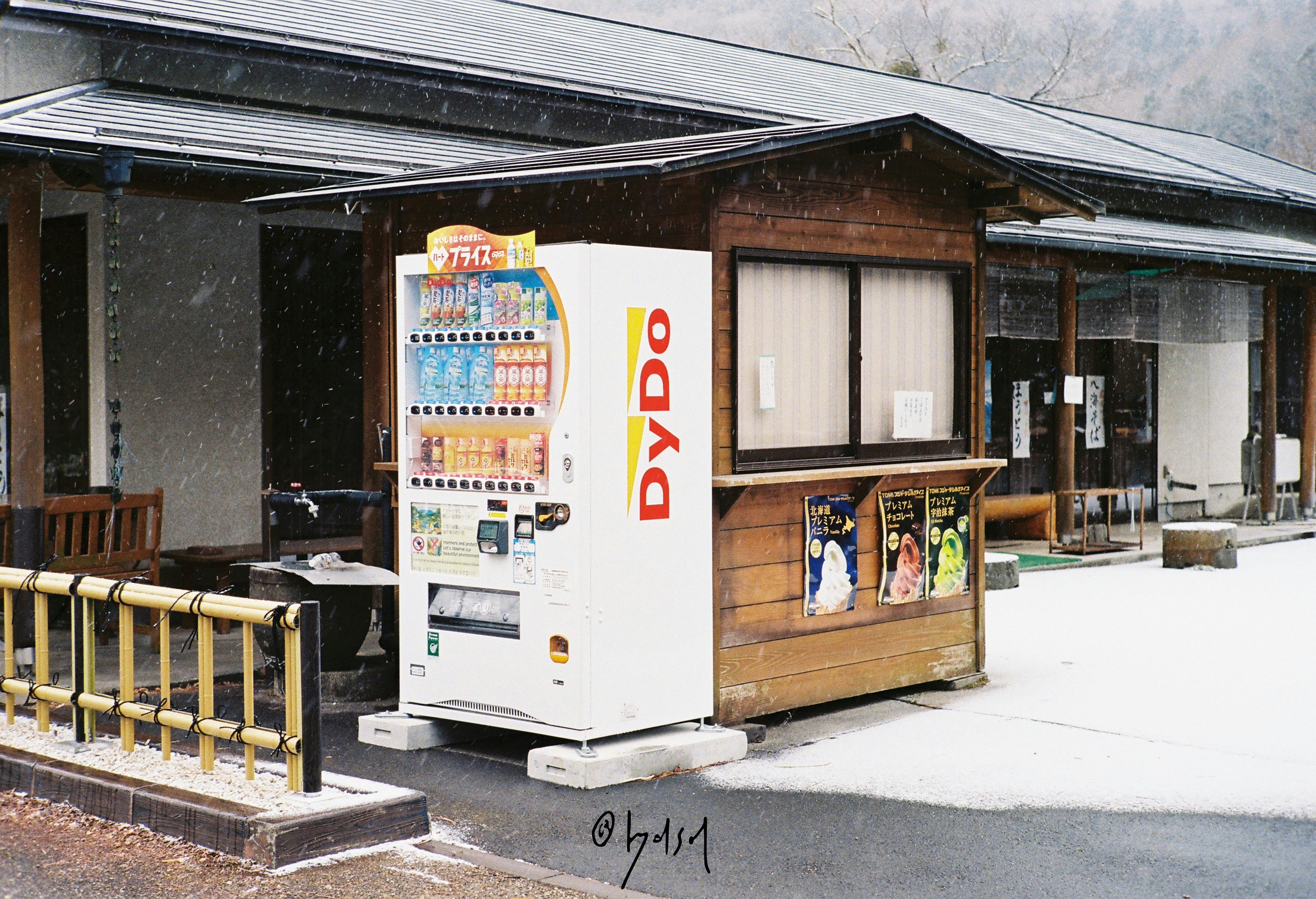 雪の降る軒先に並ぶ自動販売機と小さな売店