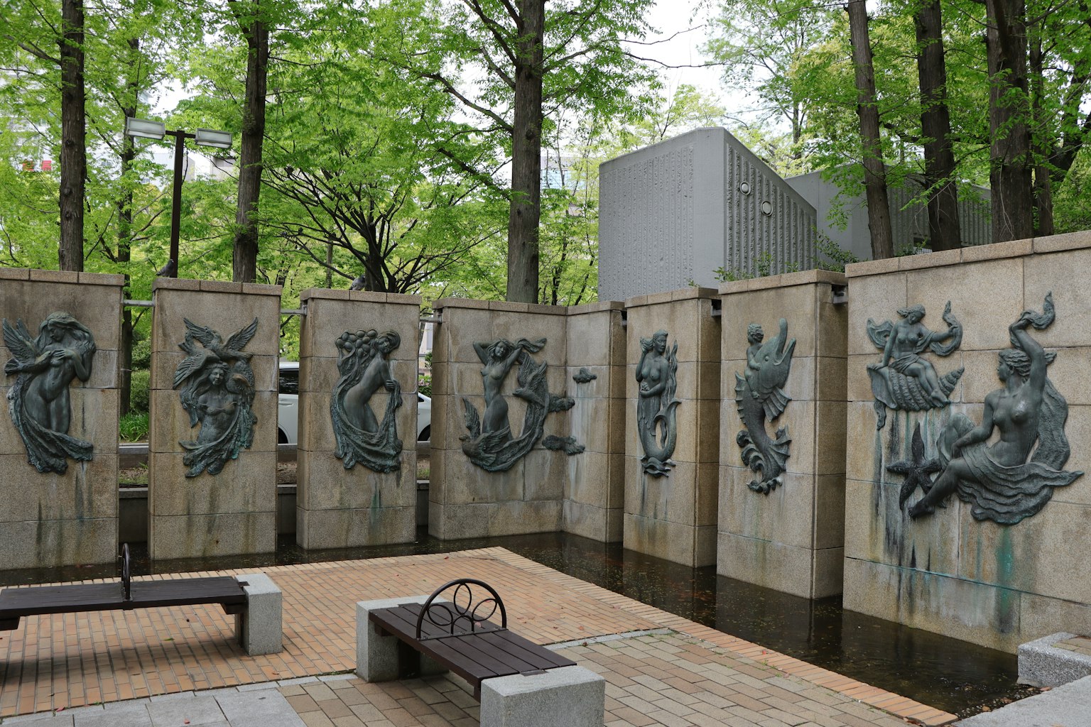 公园景观，特色雕塑墙，周围环绕着绿色树木和长椅
