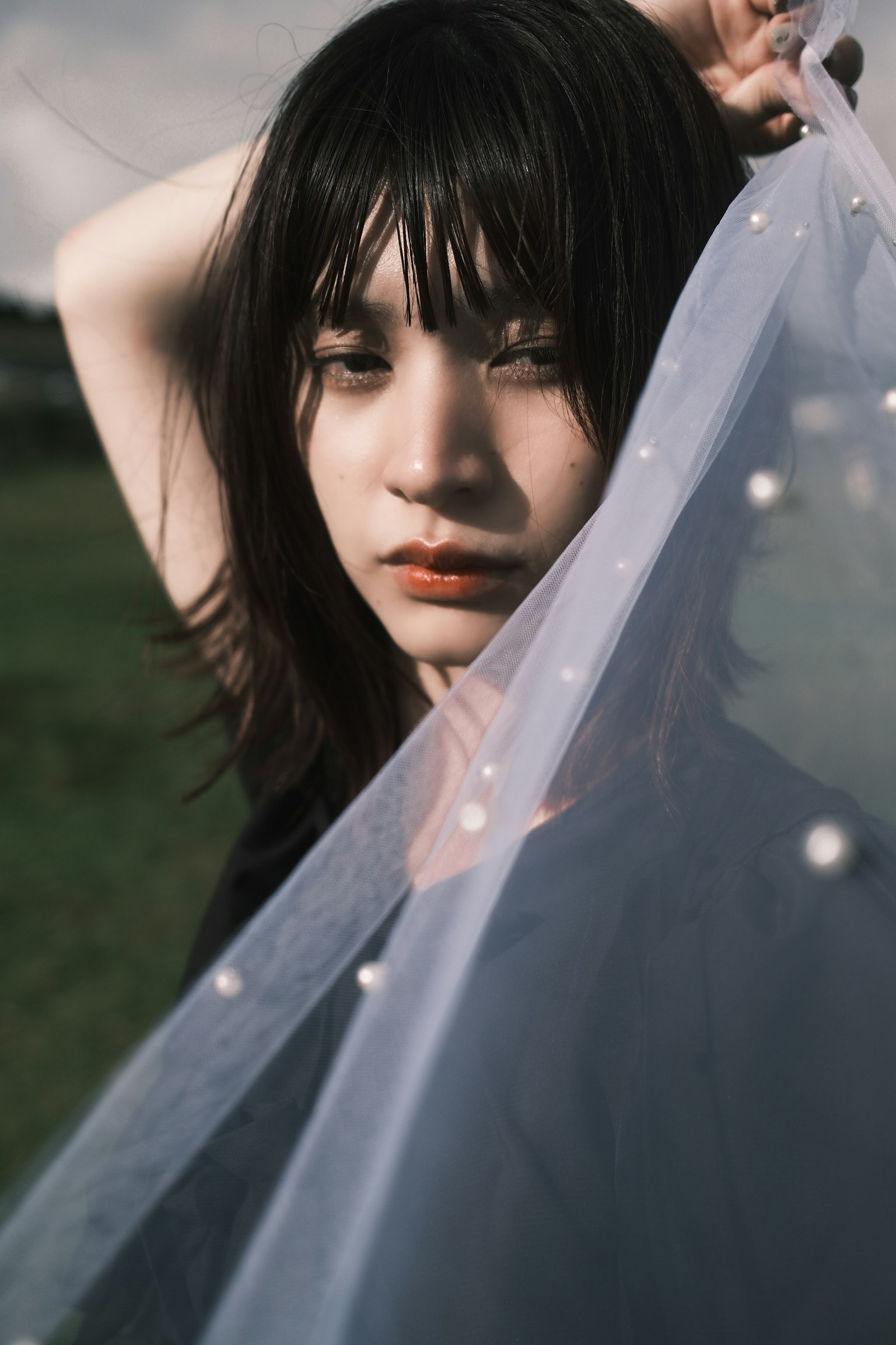 女性が薄い布を持ち上げているポートレート 自然光の中での柔らかい表情