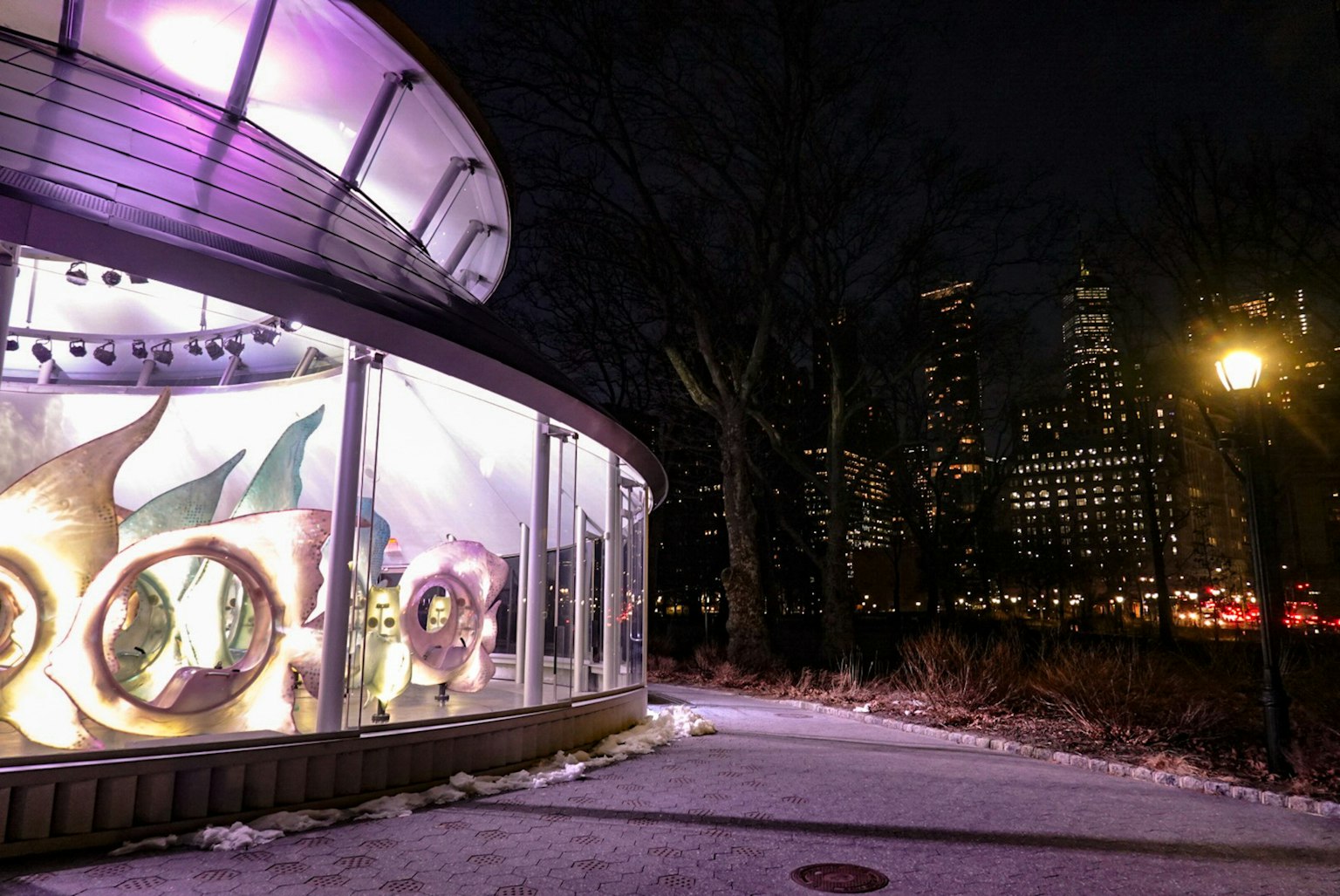 Spazio espositivo in vetro illuminato di viola contro uno skyline notturno