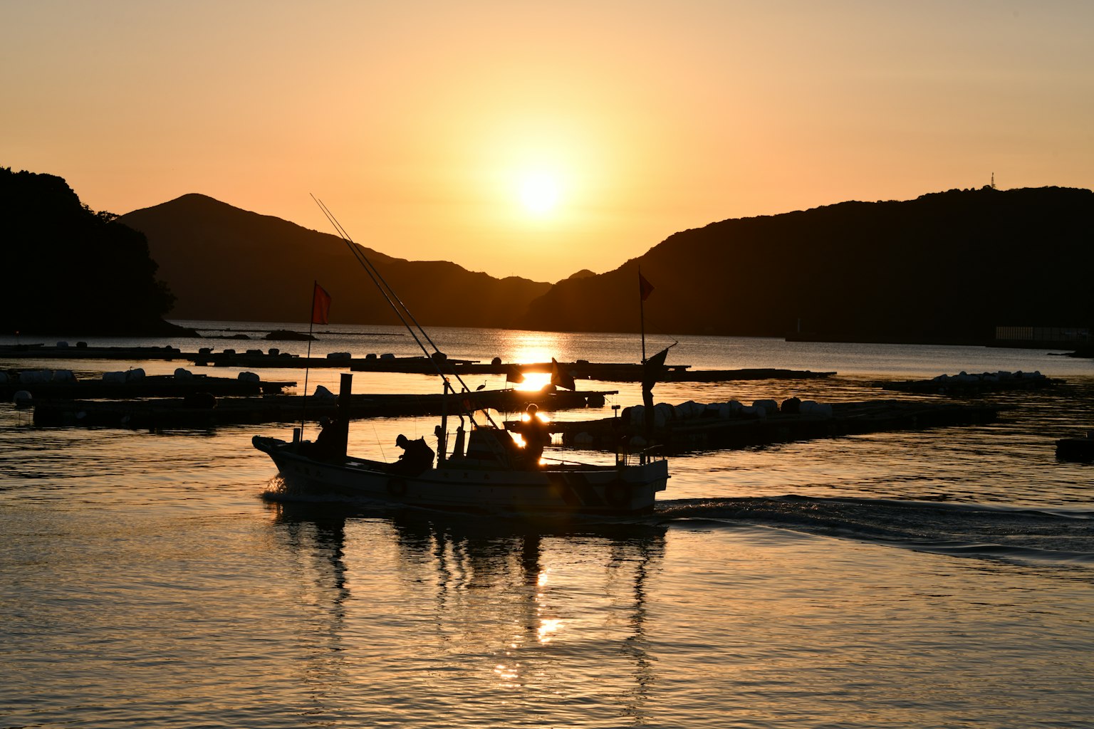 Một chiếc thuyền trôi trên mặt nước lúc hoàng hôn với những ngọn núi silhouetted