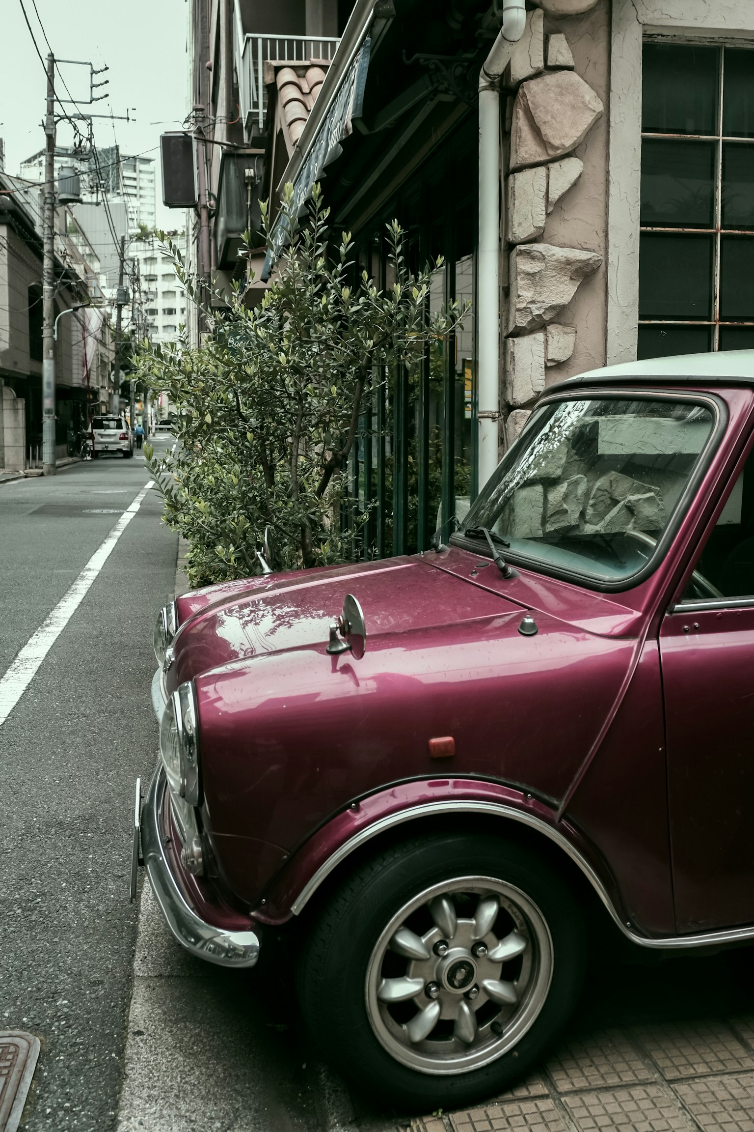 A classic maroon car parked at a street corner with greenery