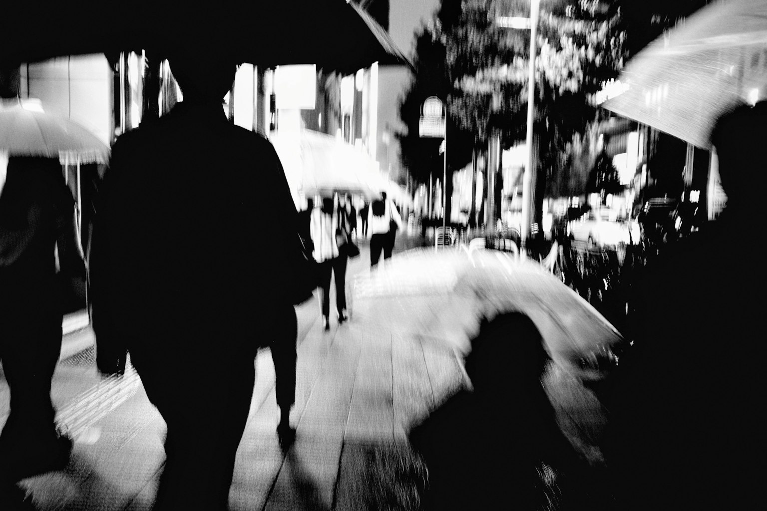 夜晚在城市街道上走的人们的剪影，手持雨伞