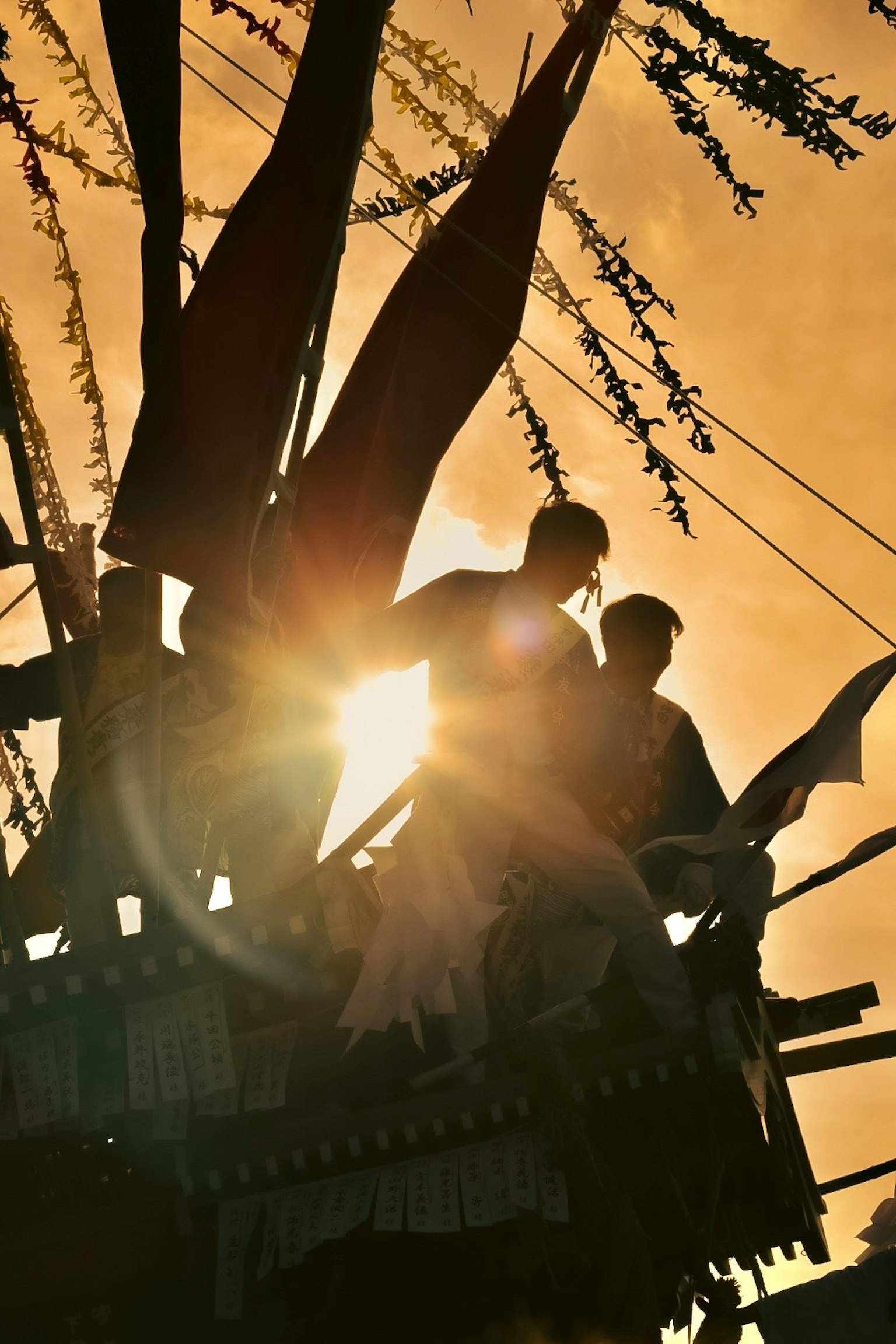 夕日を背にした二人の人物が旗の近くに立っているシルエット