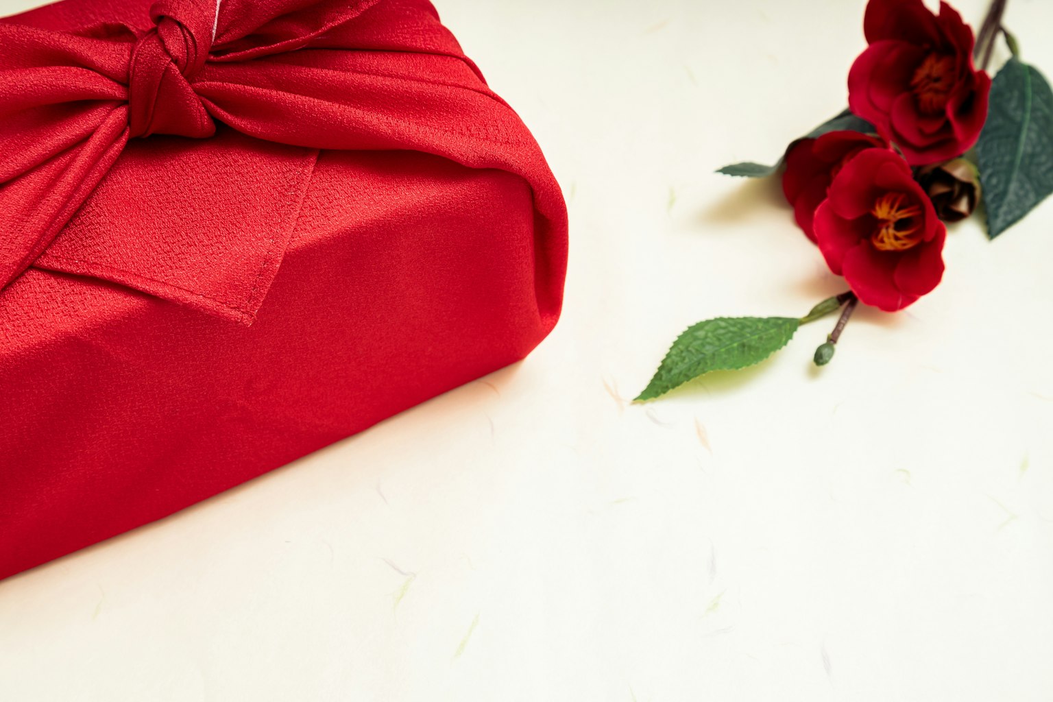 Regalo envuelto en rojo con un lazo y flores rojas sobre un fondo simple