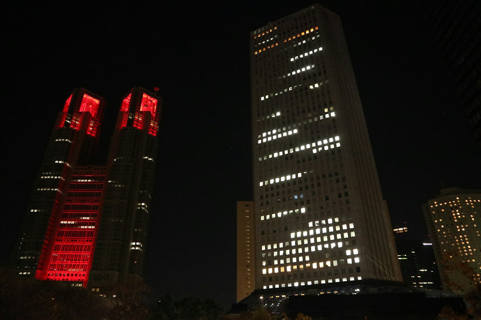 Gedung pencakar langit Tokyo di malam hari dengan menara kembar bercahaya merah dan jendela yang terang