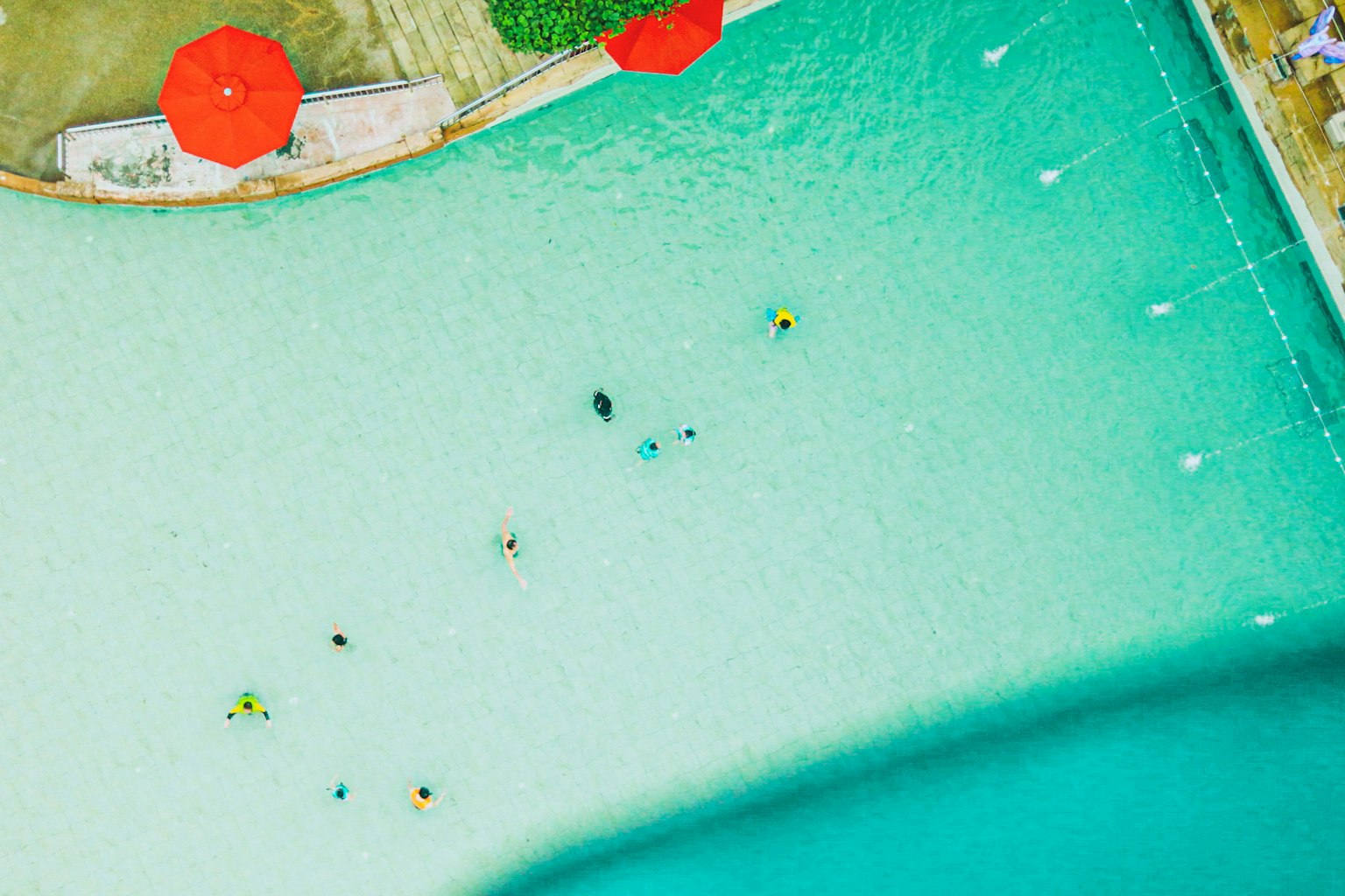 Vista aérea de personas nadando en agua turquesa con sombrillas rojas