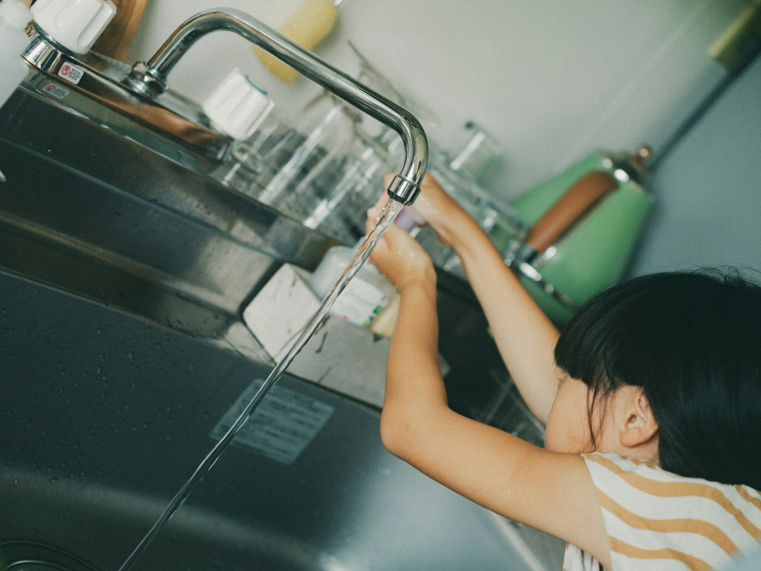 子供がキッチンの蛇口から水を出している様子