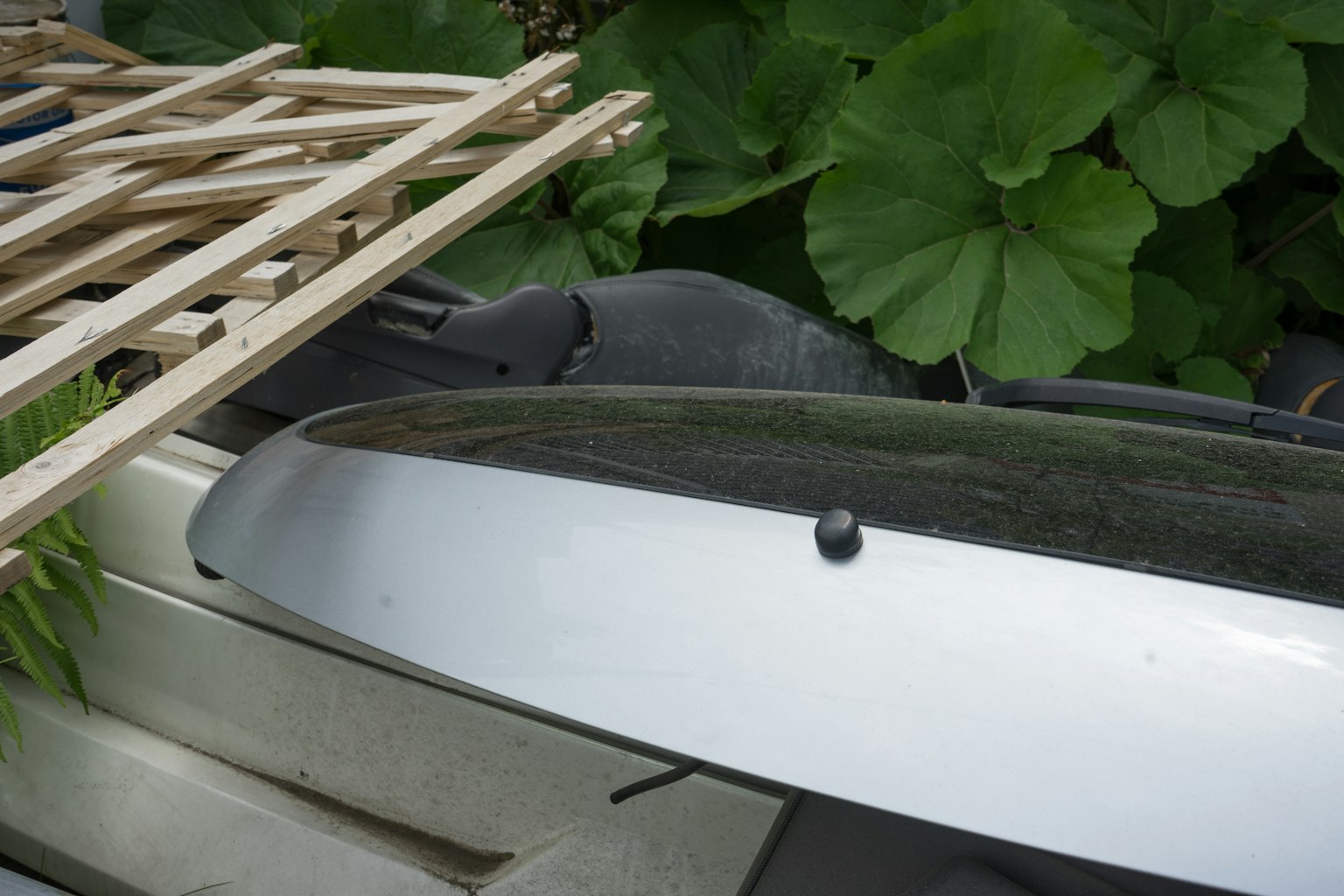 Silver object partially covered by wooden slats against a green leafy background