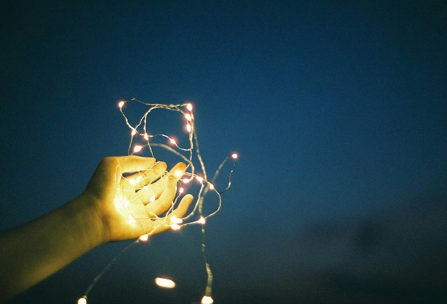 Silueta de una mano sosteniendo luces brillantes contra un cielo crepuscular