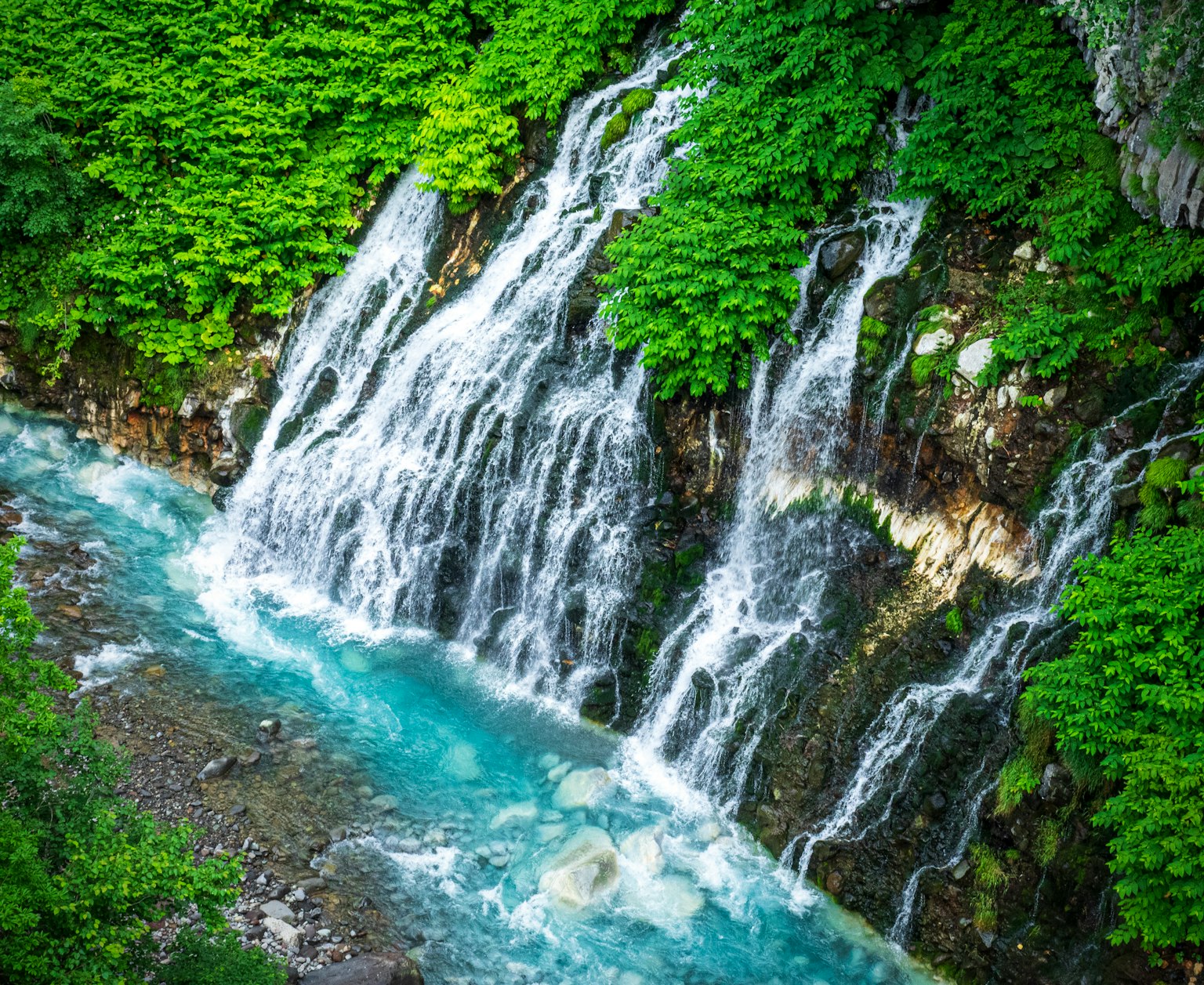 Air terjun yang indah mengalir ke sungai turquoise dikelilingi oleh dedaunan subur
