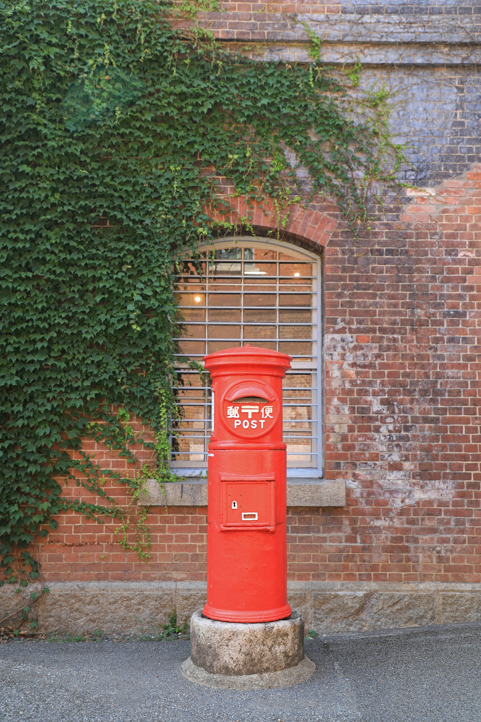 Red mailbox standing in front of a brick wall with green ivy