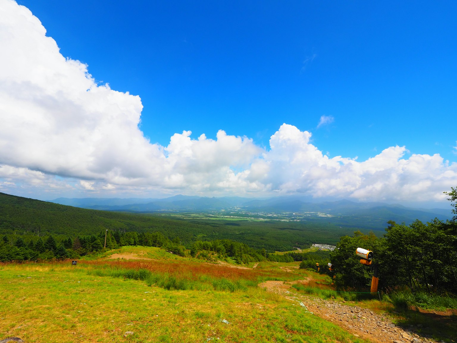 Panoramablick auf eine grüne Landschaft und Berge unter einem blauen Himmel mit weißen Wolken