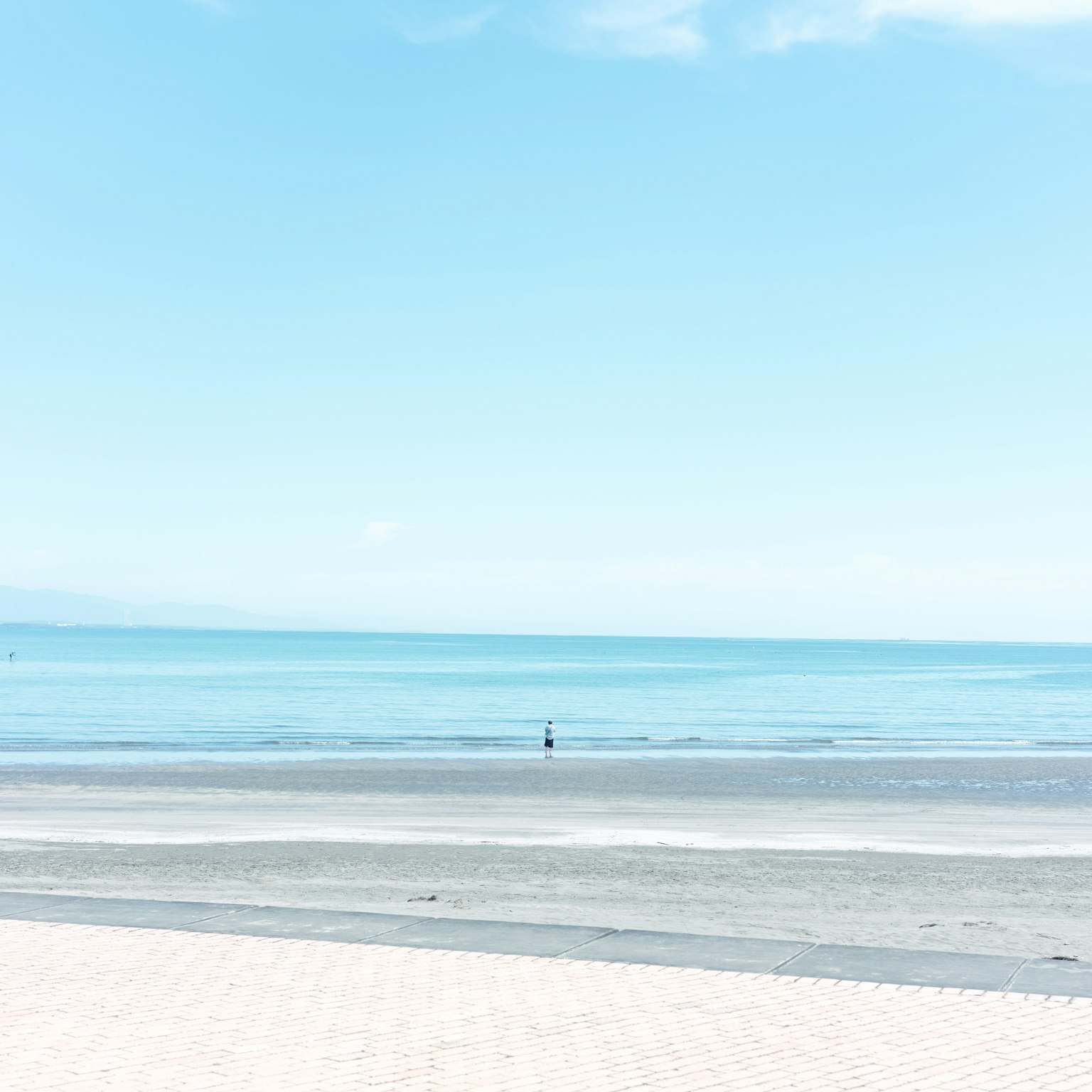 Pemandangan pantai yang tenang dengan laut dan langit biru yang tenang Seseorang berdiri di kejauhan