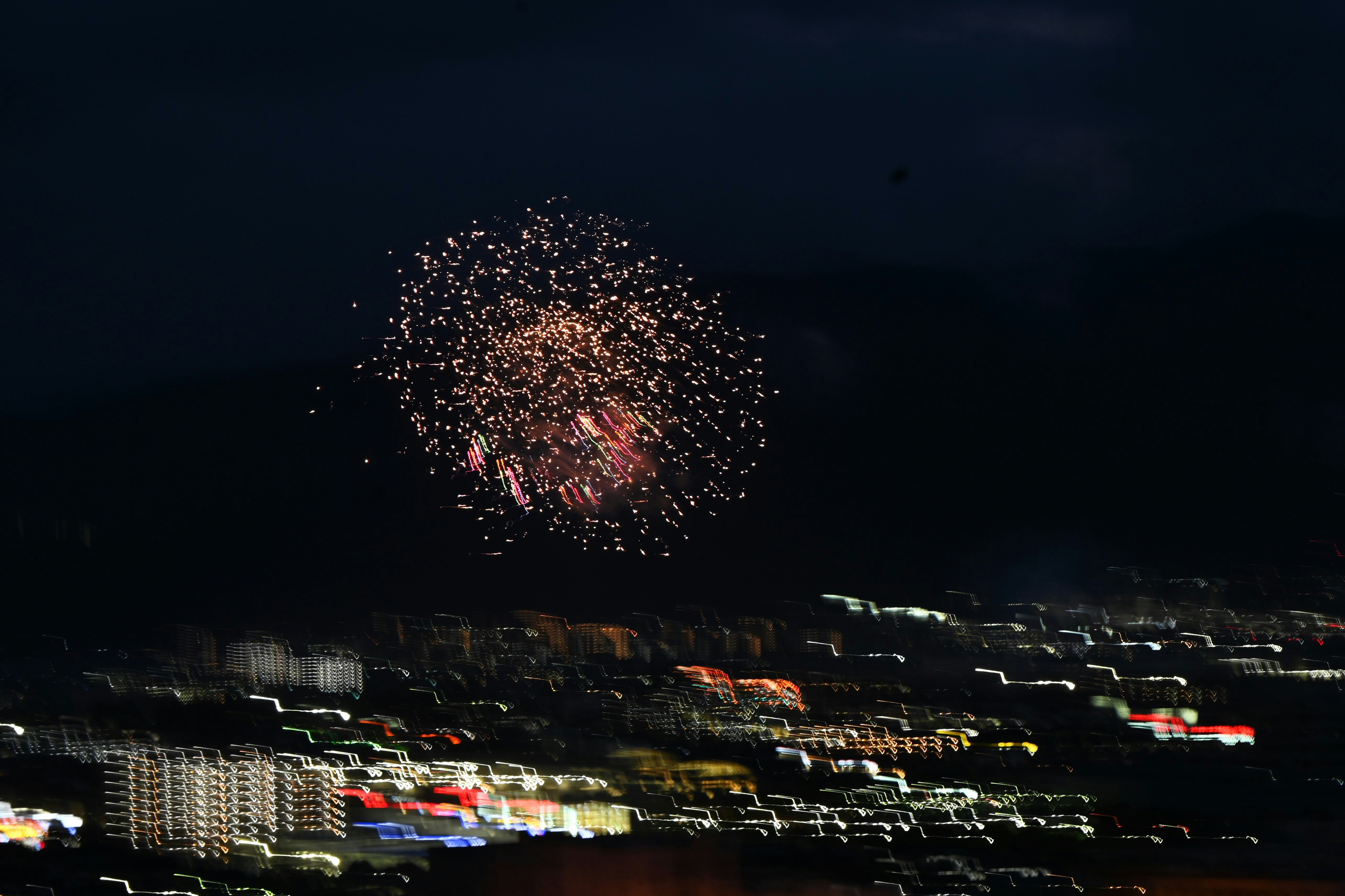 夜空に広がる花火と街の光が並ぶ海辺の夜景