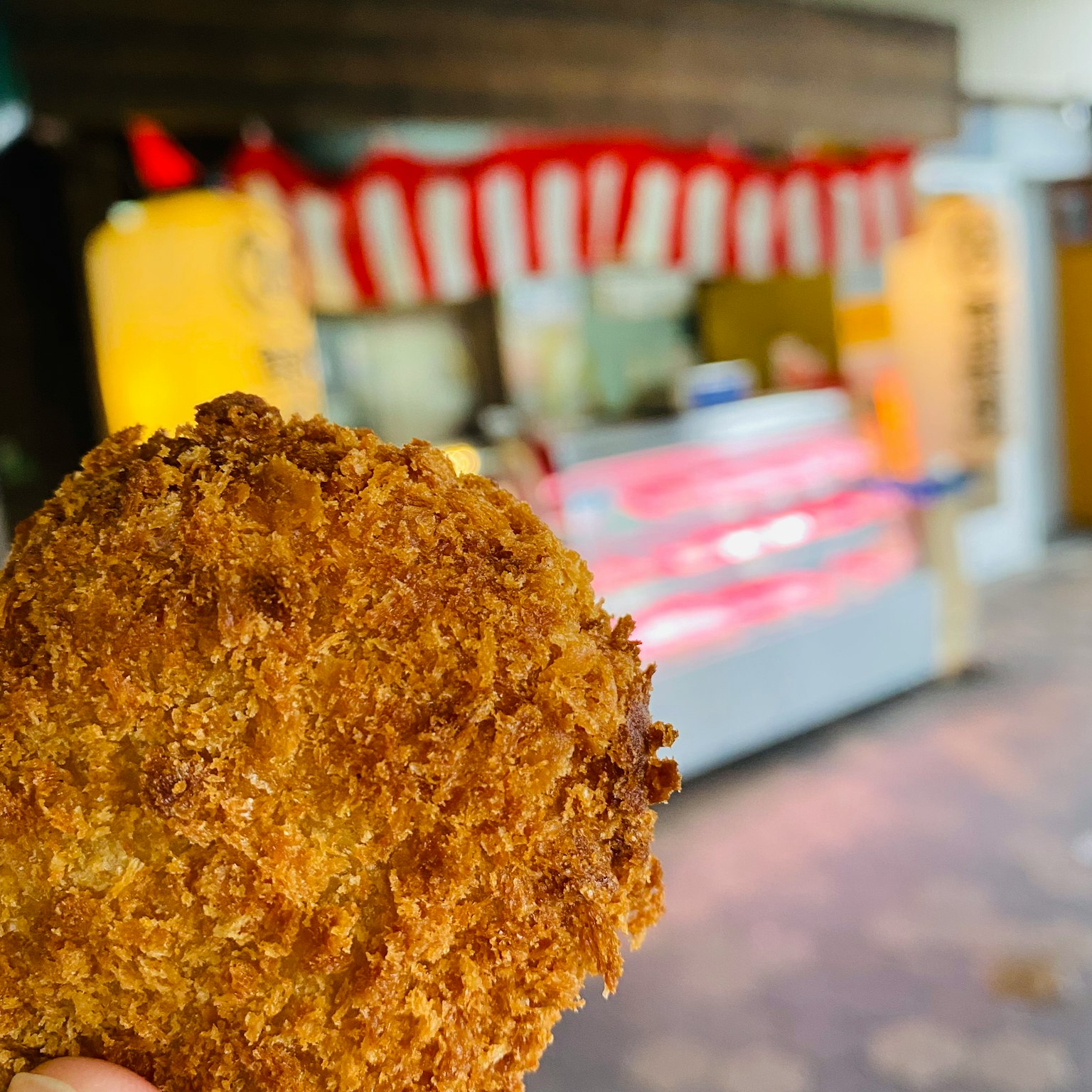 手中拿著新鮮炸製的可樂餅，背景是一個食品攤位