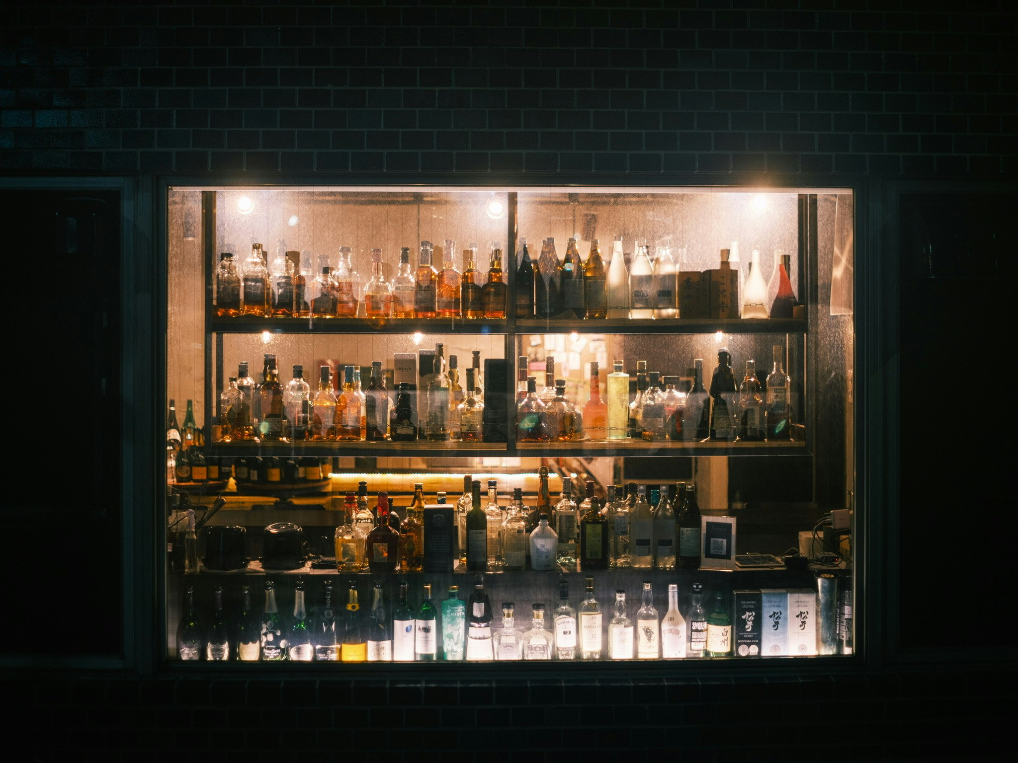 Flaschen und Gläser auf einer Bar-Theke vor einer Ziegelwand