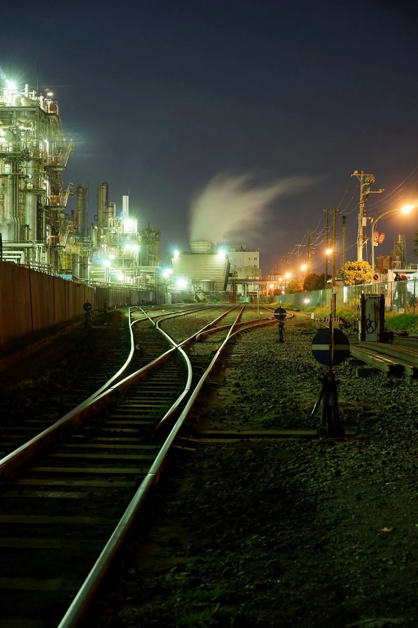 夜の線路と工場の灯りが並ぶ貨物駅の風景