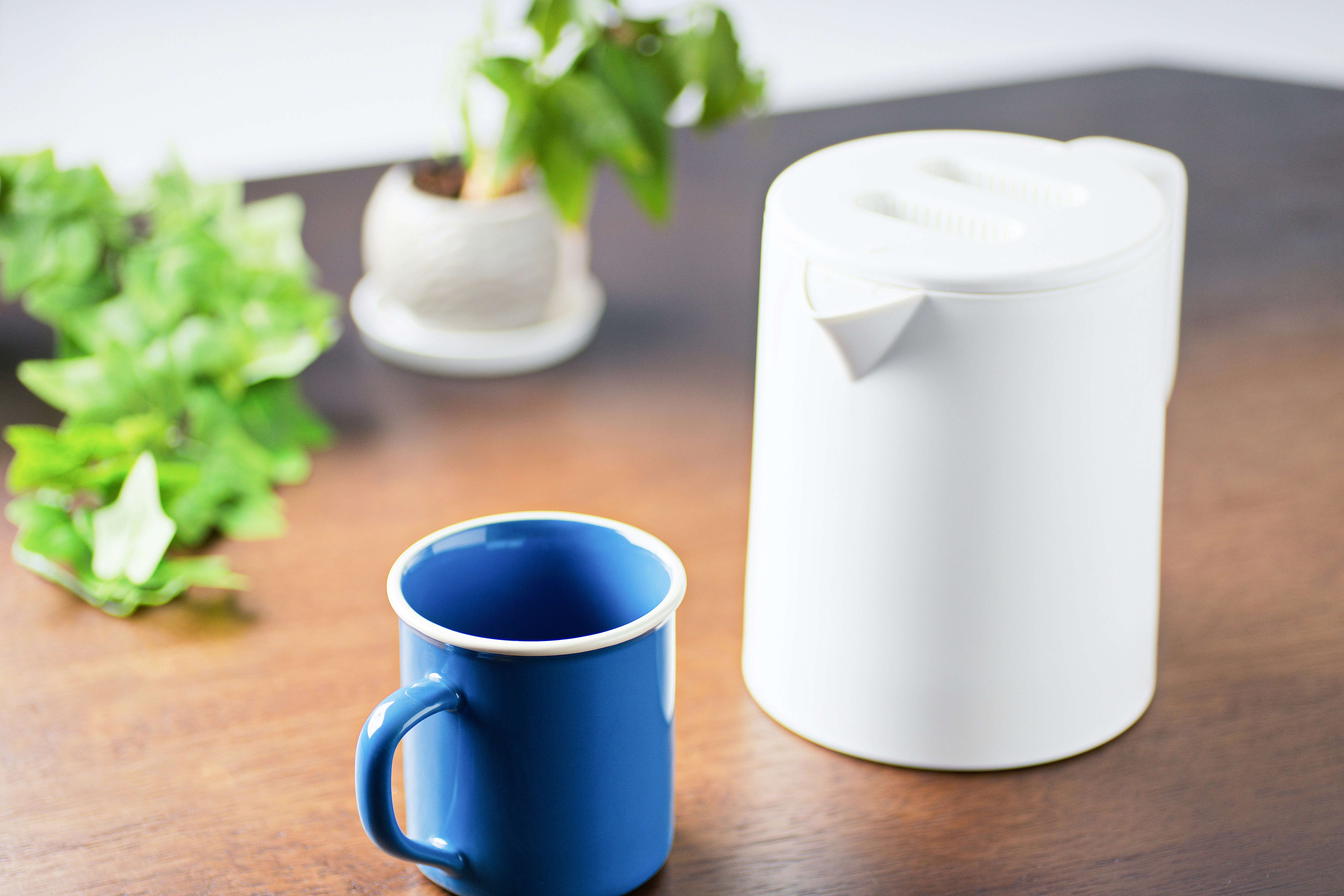 朝日を浴びる木のテーブルの青いマグカップとケトル