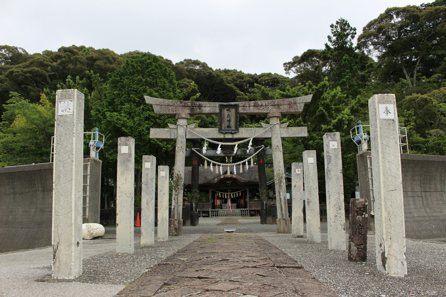 Eingang eines Schreins mit einem Torii und Steinsäulen, umgeben von üppigem Grün