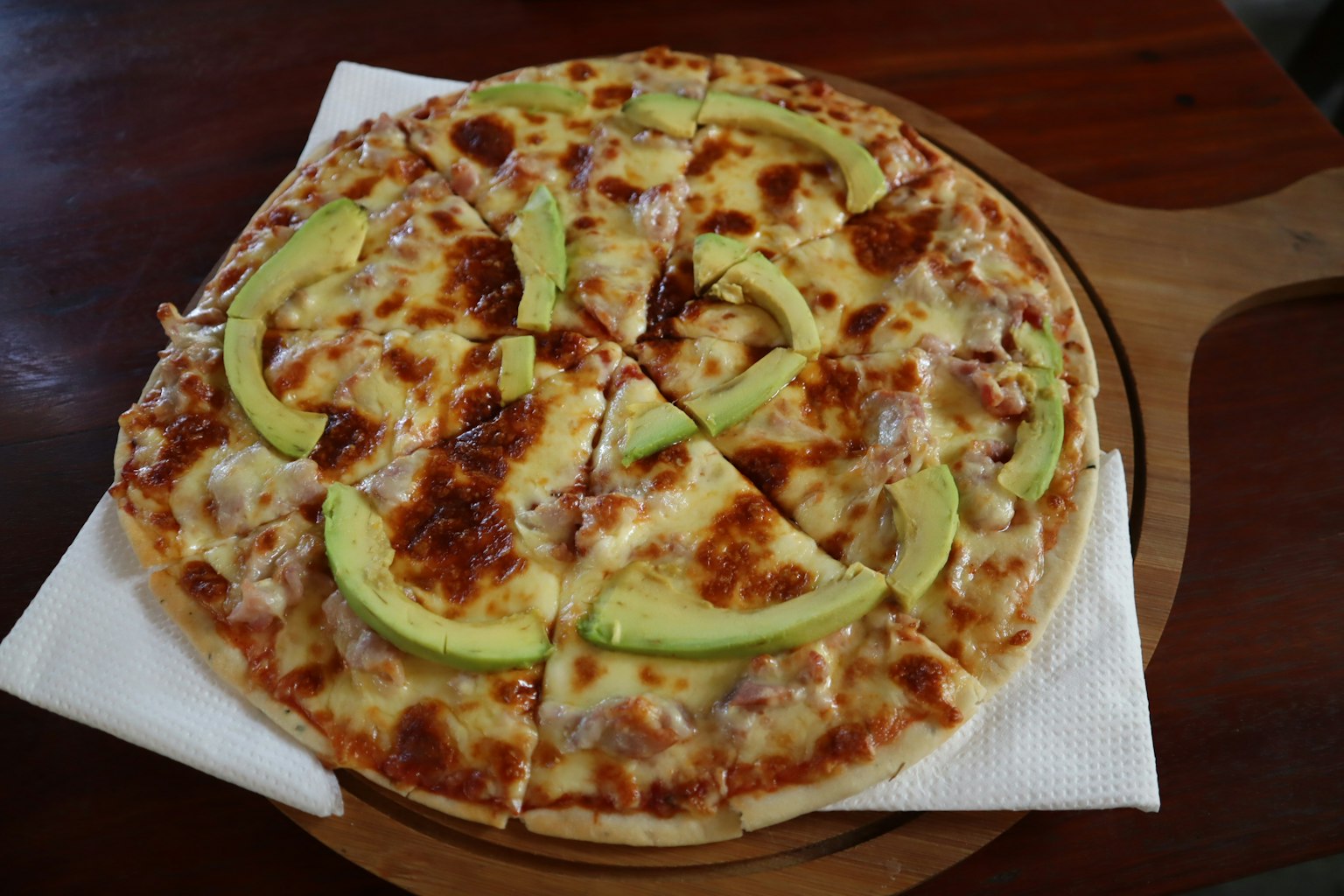 Pizza dengan irisan alpukat di atas papan kayu