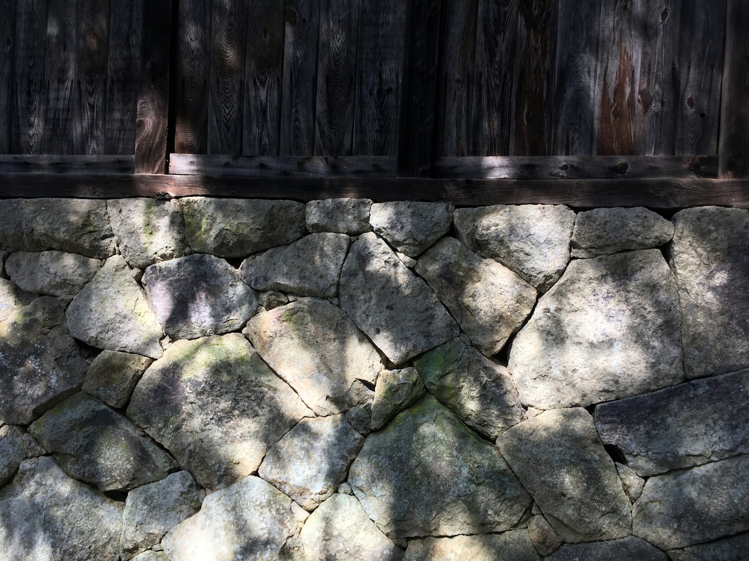 Textura detallada de una pared de piedra con sombras frente a una pared de madera