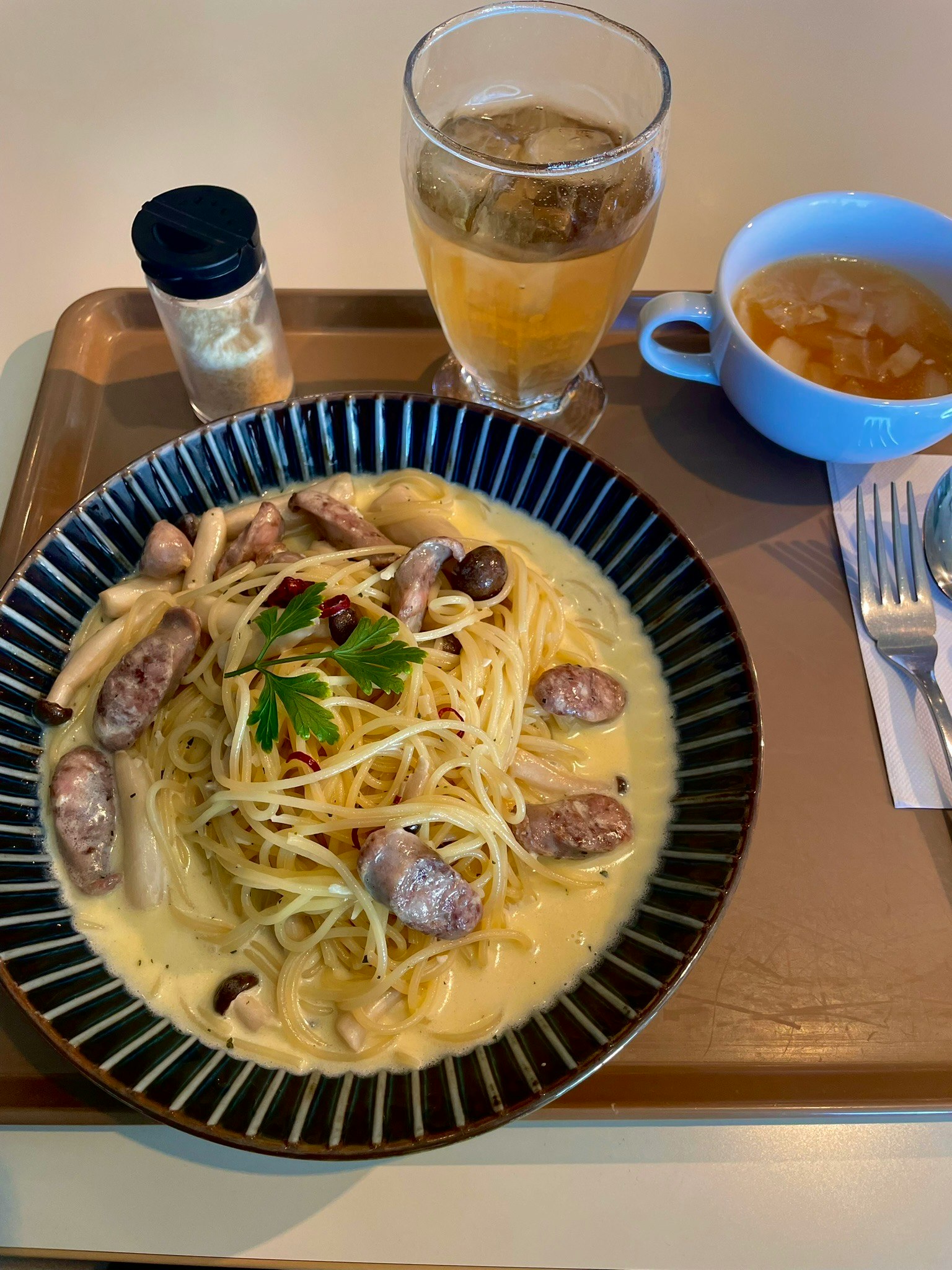 A plate of pasta with sausage garnished with parsley served alongside a drink and soup