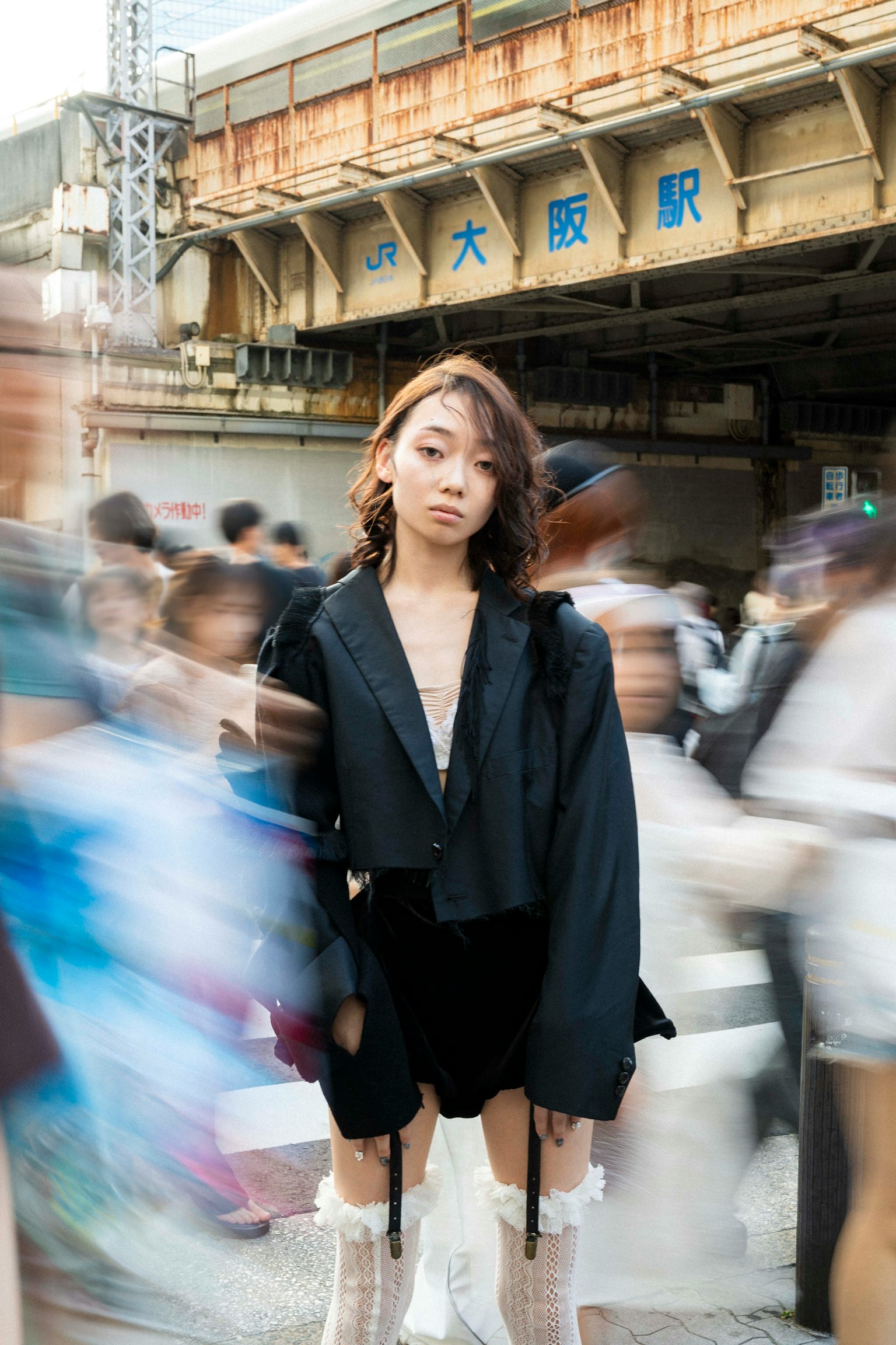 Fashion photo of a woman standing amidst a crowd with Osaka Station blurred in the background