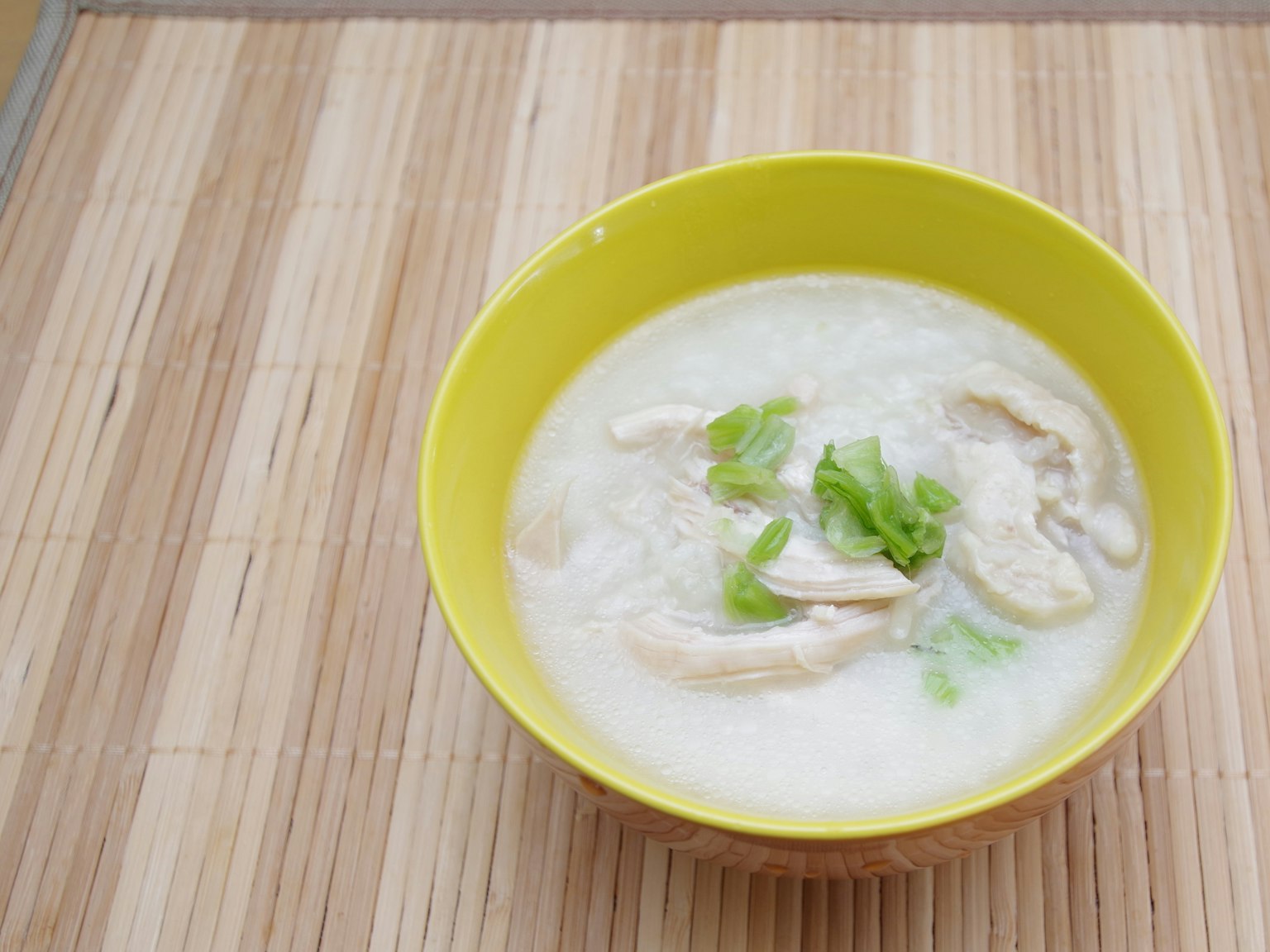 黄色碗中的鸡肉汤，配有切片鸡肉和青葱