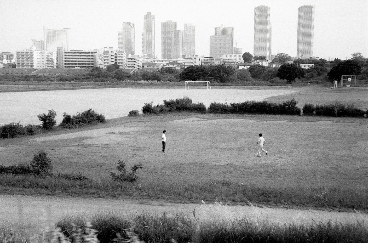 Two boys playing soccer in a field with a city skyline in the background