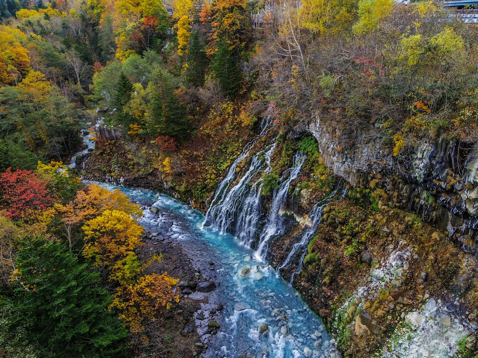 Vista panoramica di cascate e un fiume blu circondato da foglie autunnali