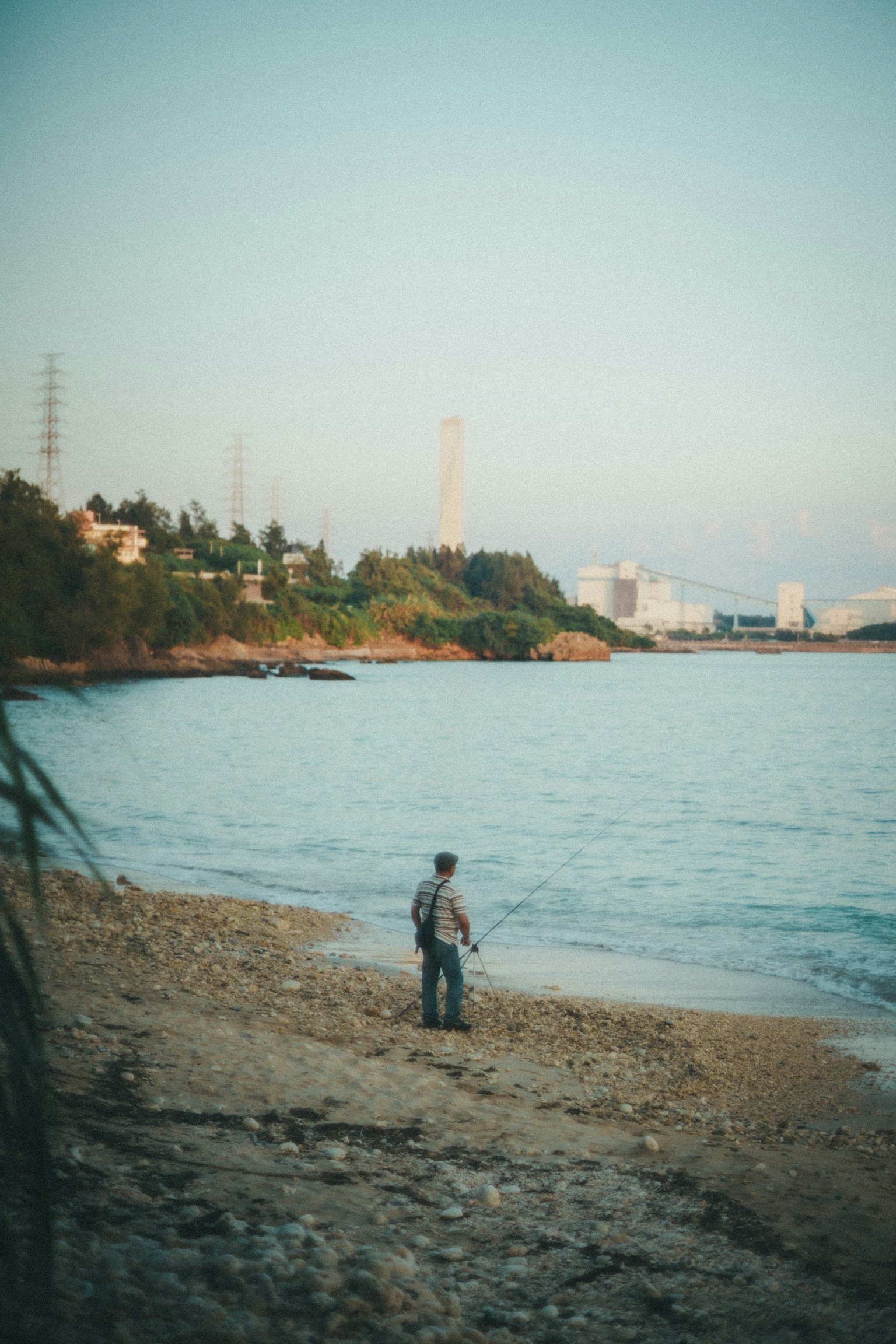 Seorang pria memancing di tepi pantai dengan gedung kota di latar belakang