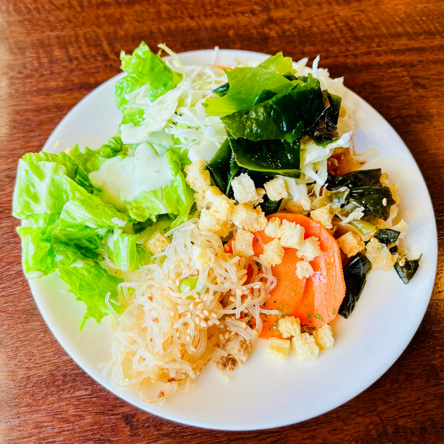 A white plate with a salad featuring green leafy vegetables and seaweed