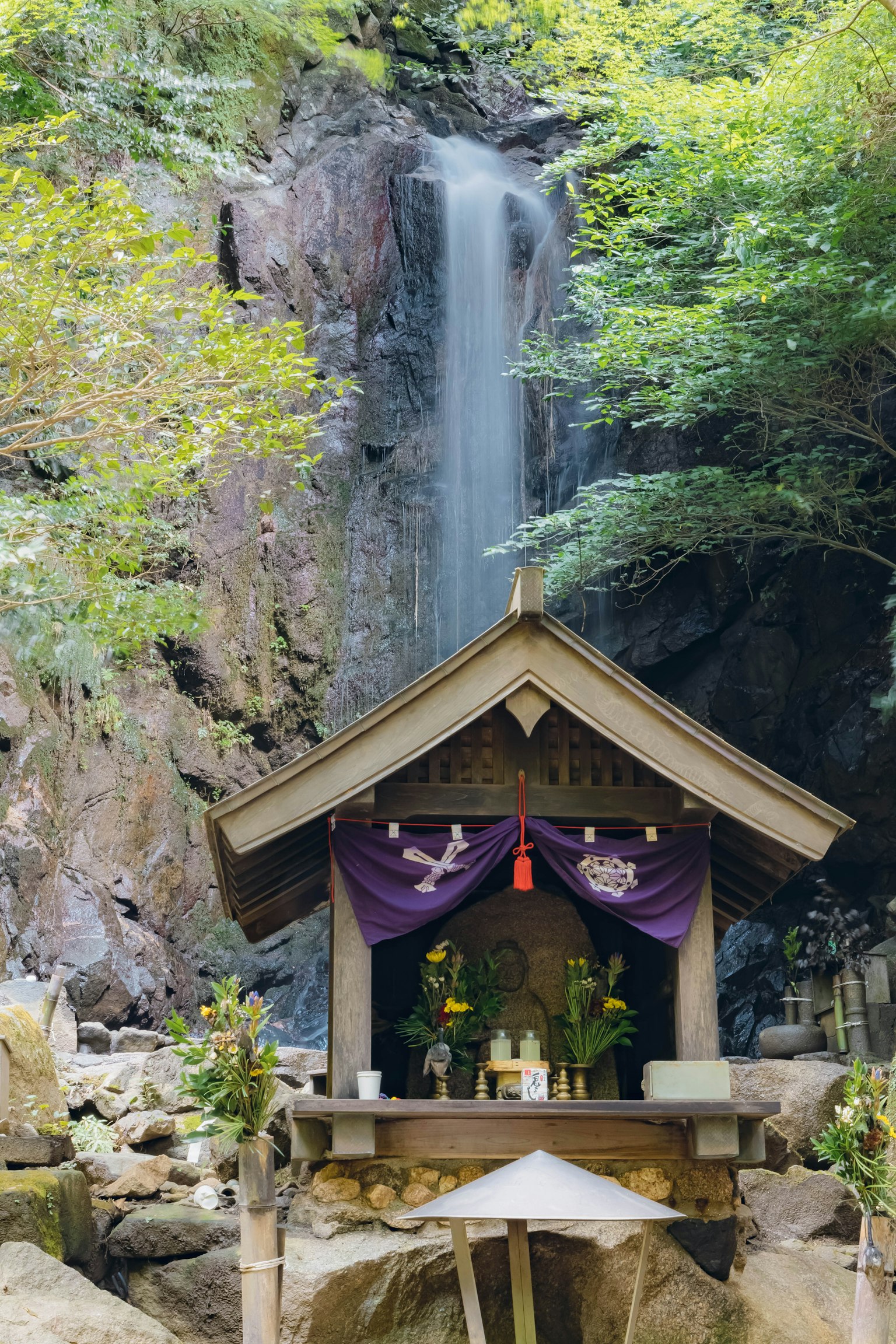 Small shrine in front of a waterfall surrounded by lush greenery