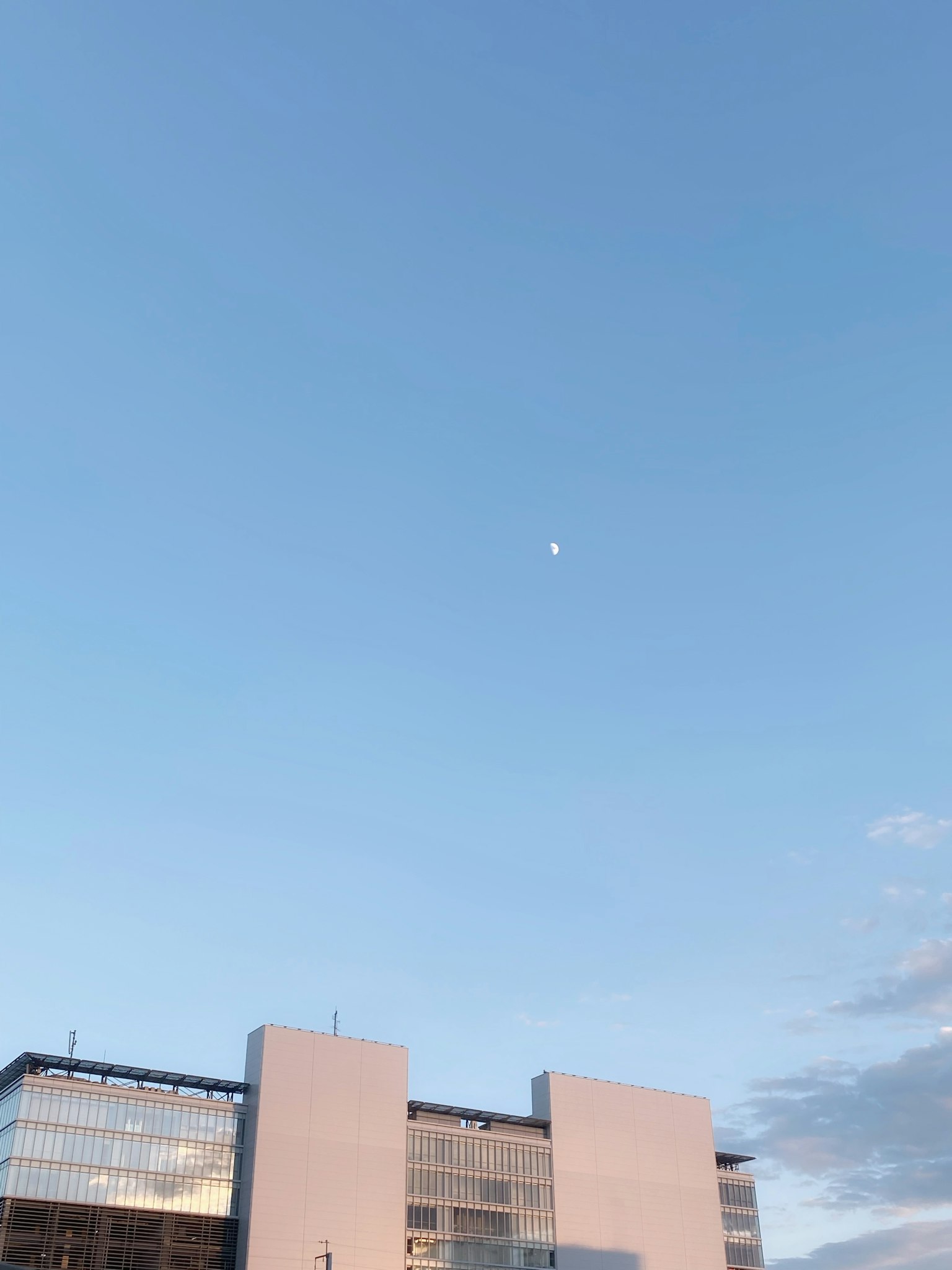 Un edificio moderno sotto un cielo blu chiaro con una luna visibile