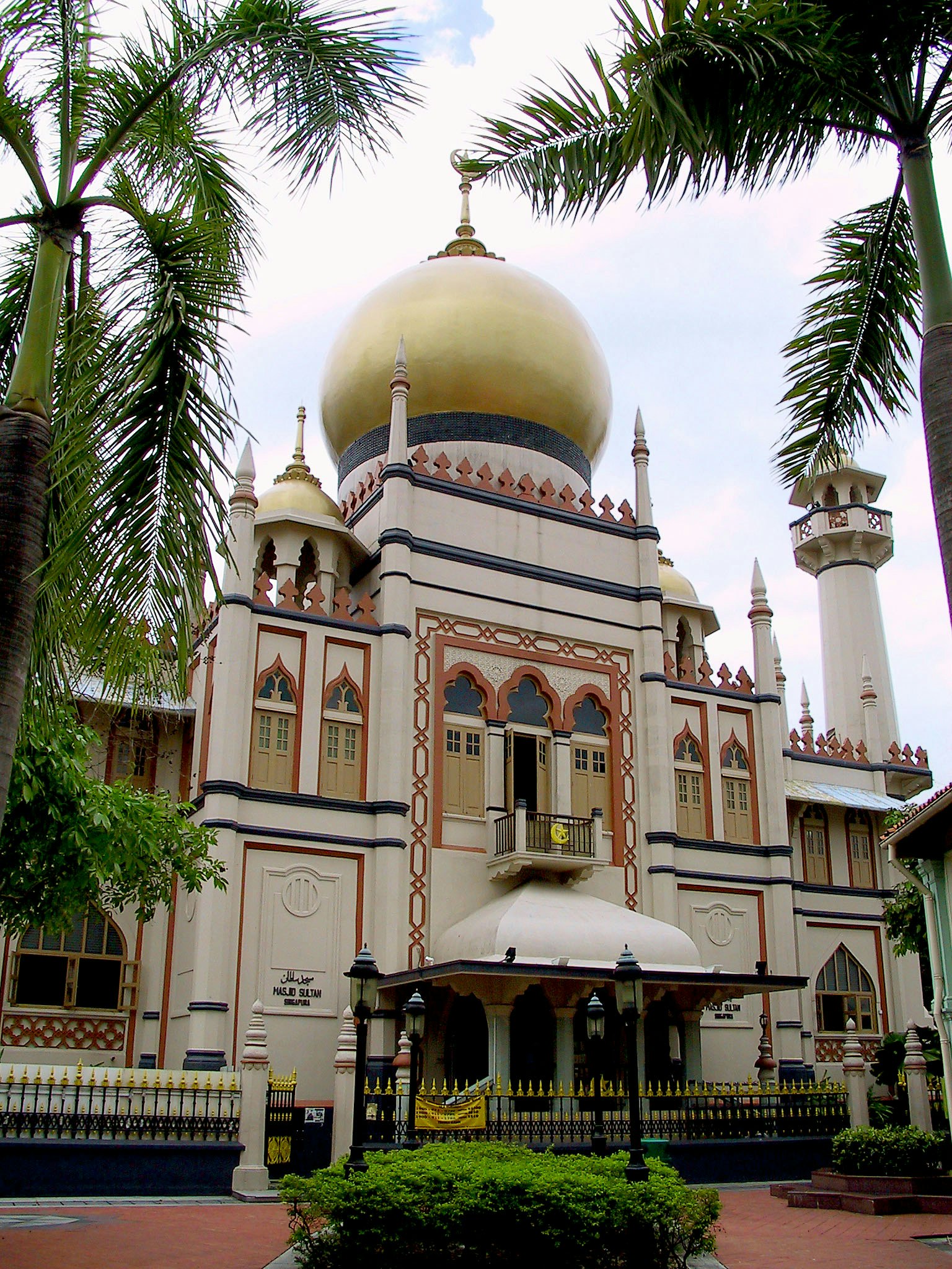 Esterno di una moschea con una cupola dorata e decorazioni intricate circondata da vegetazione