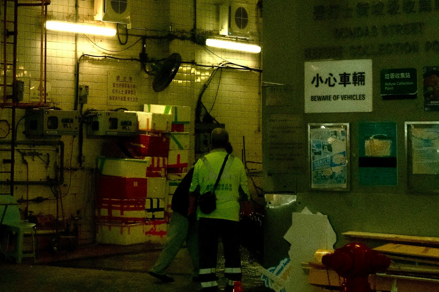 夜の小さな車両用通路で作業する人と掲示板のある壁面