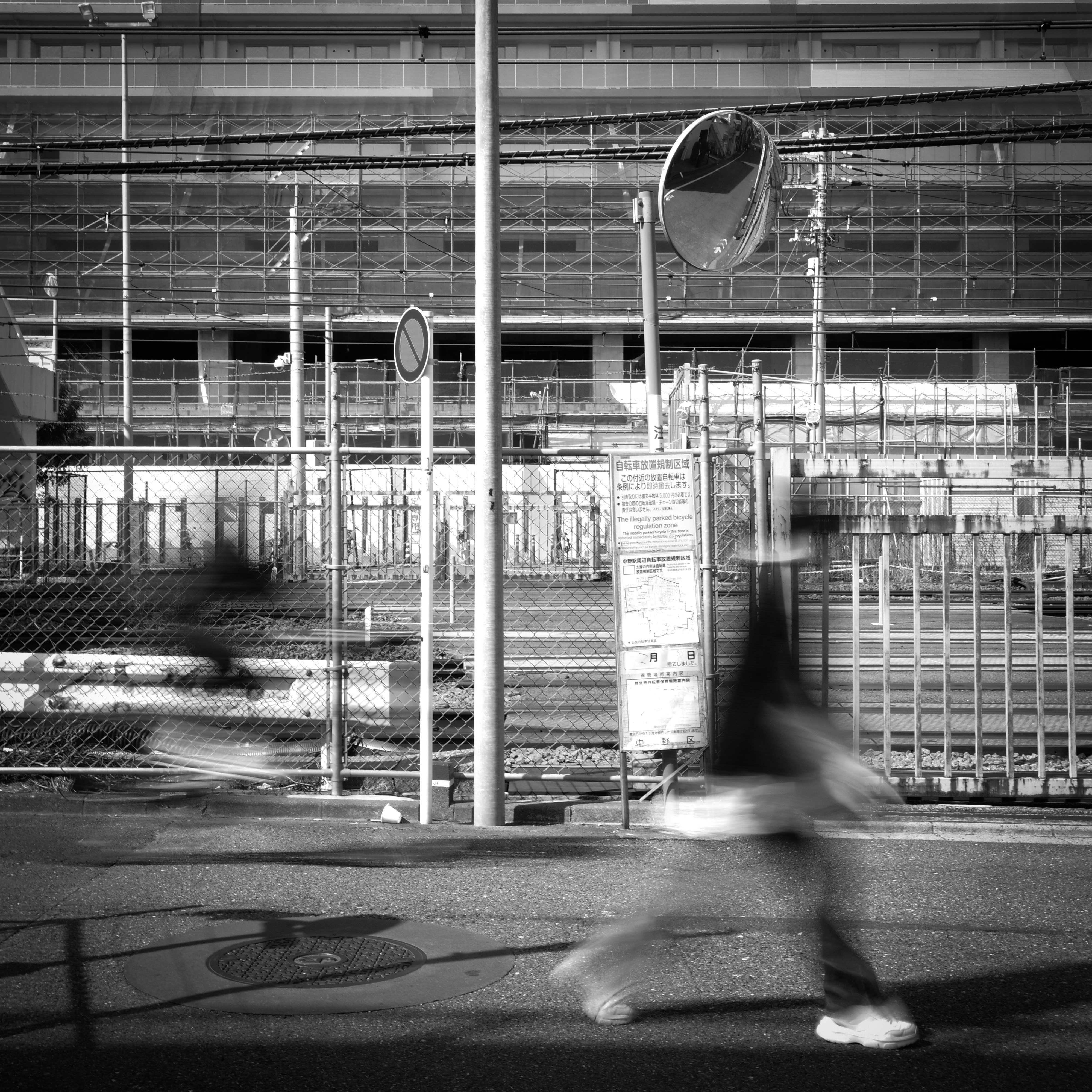東京のモノクロで工事フェンスと歩行者のある高架沿いの風景