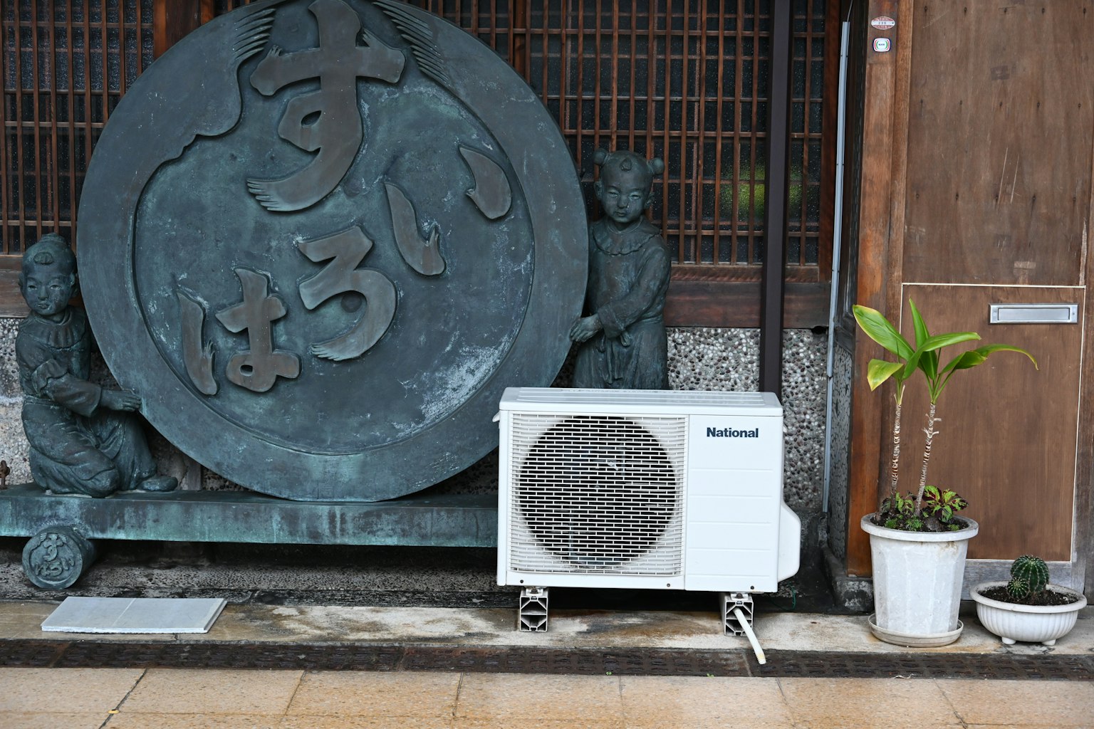 Patung batu besar dengan karakter Jepang di samping unit pendingin udara