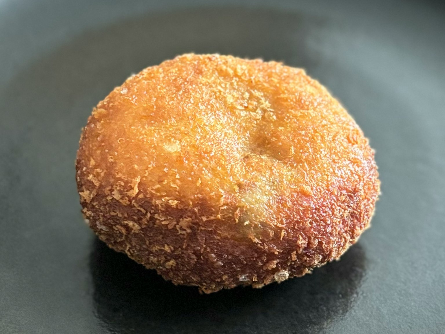 Uno snack rotondo fritto simile a un donut su un piatto nero