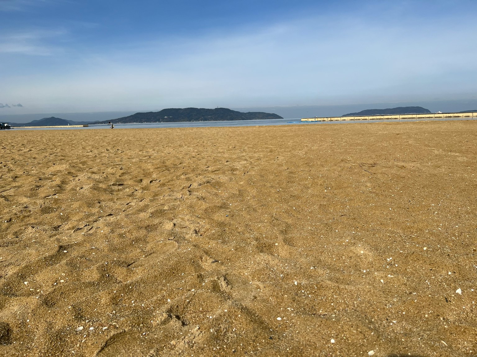 Wide sandy beach with distant islands under a blue sky