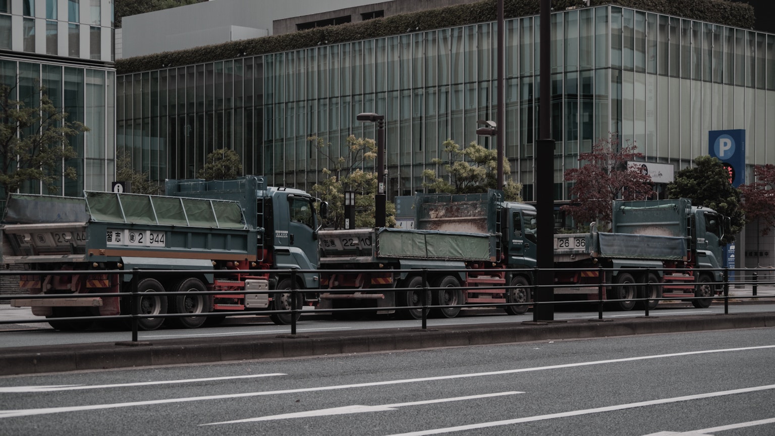 Flotta di camion parcheggiati in una strada urbana con un edificio in vetro moderno sullo sfondo
