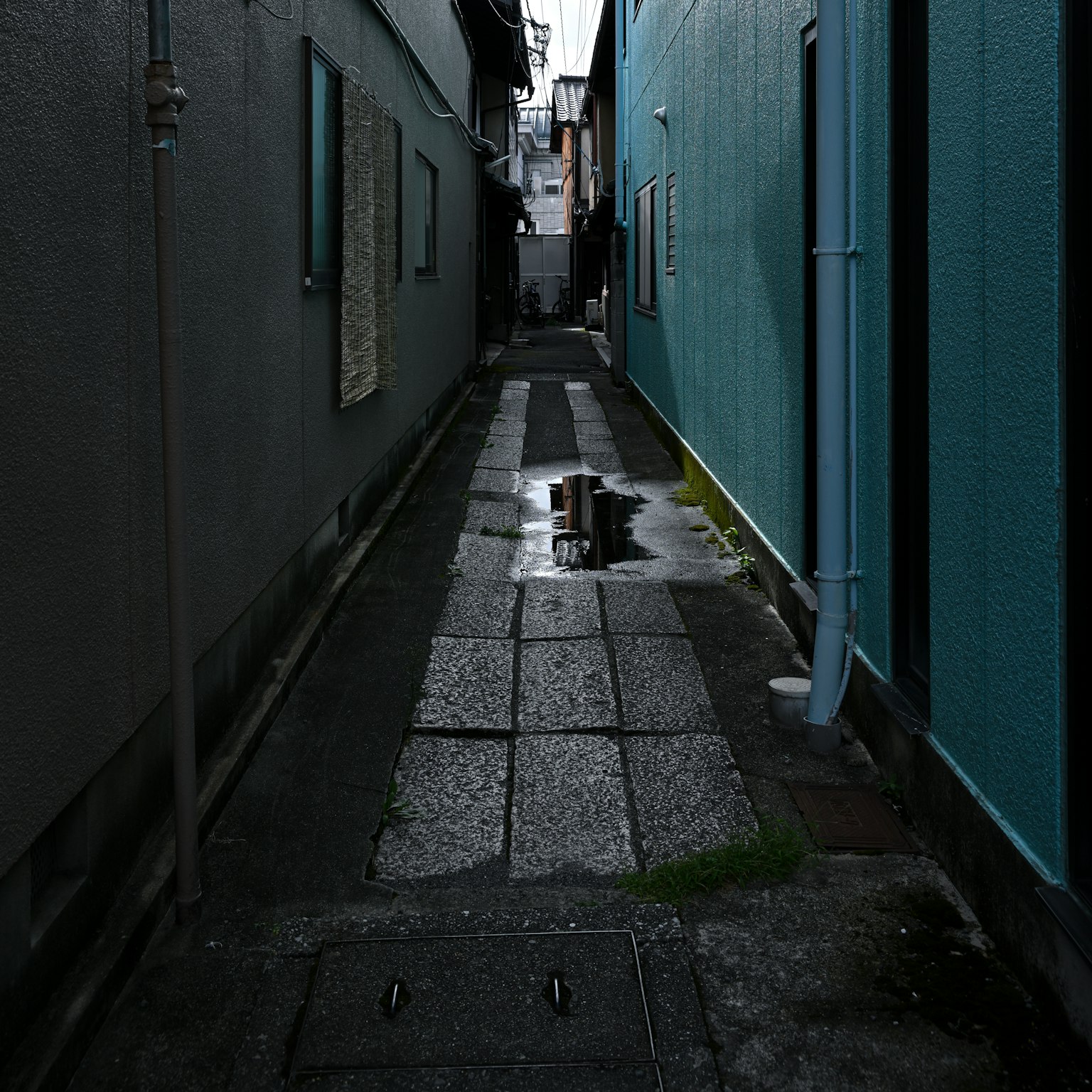 狭い路地に水たまりが映る風景 青い壁と暗い建物が特徴的