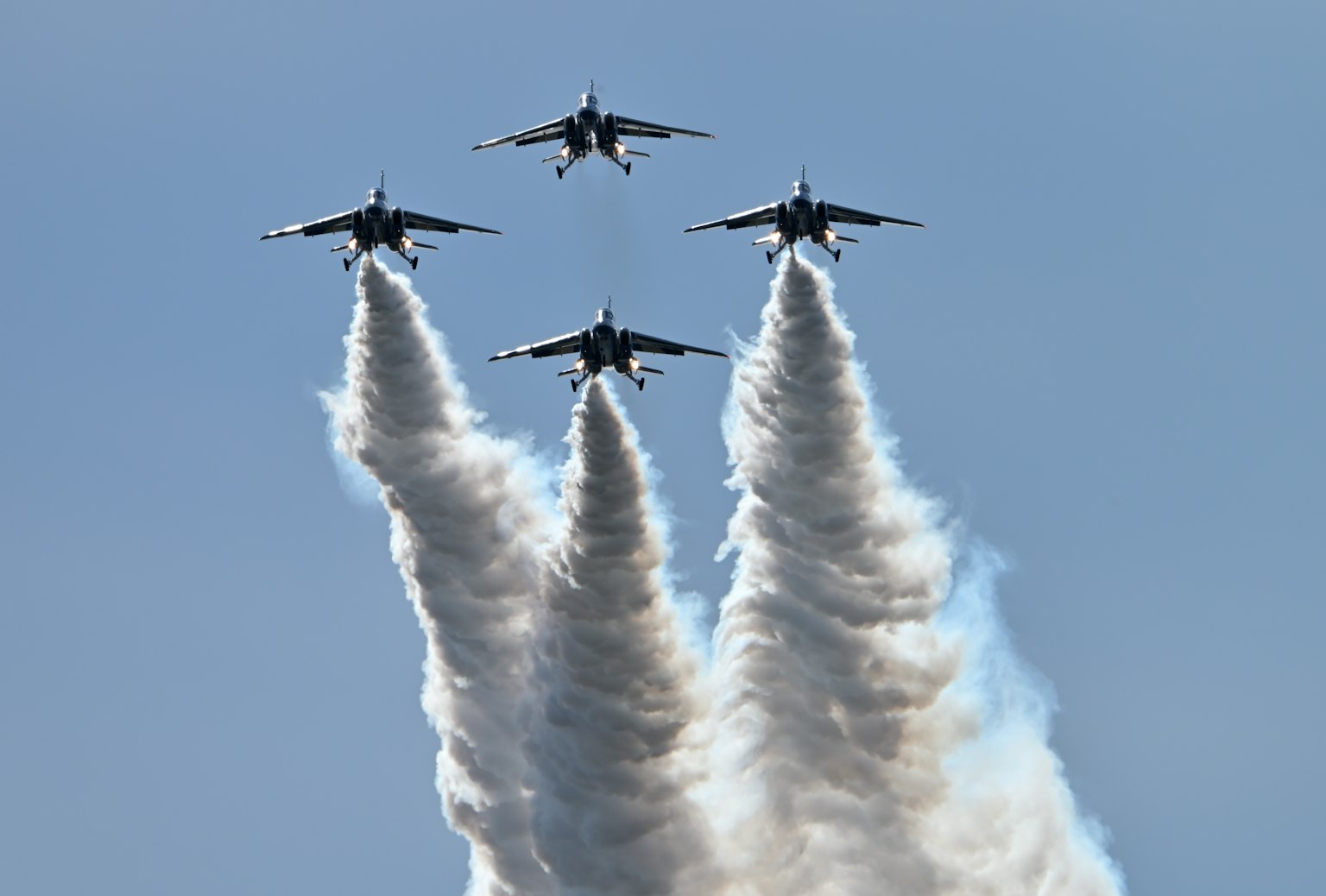 Vier Kampfflugzeuge fliegen in Formation und hinterlassen Rauchspuren