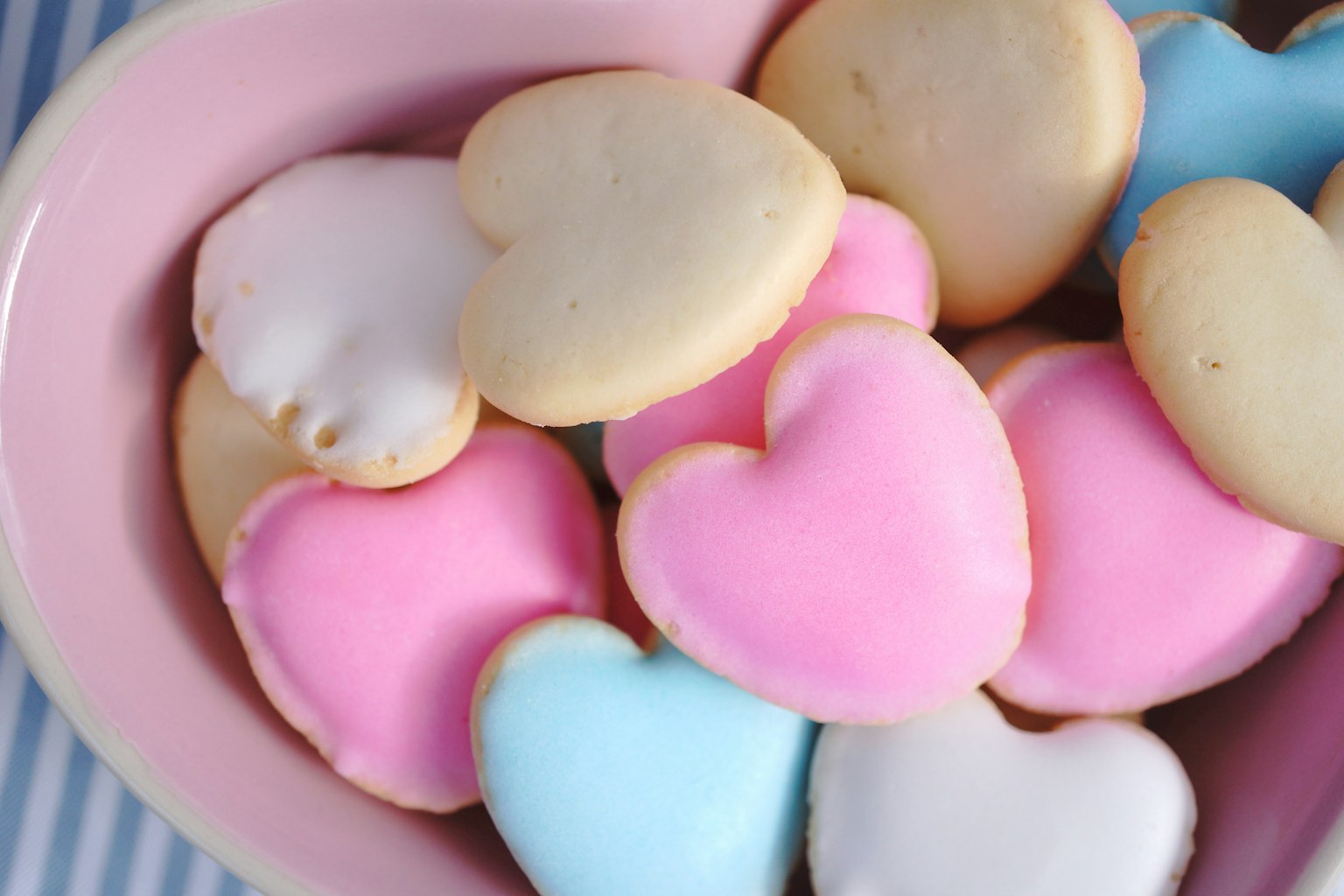 Heart-shaped cookies decorated with pink and blue icing in a pink bowl